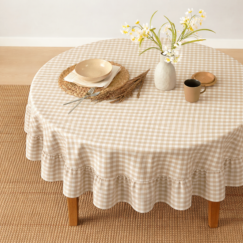 Round table with a checkered tablecloth, plates, cups, and flowers on a wooden floor.