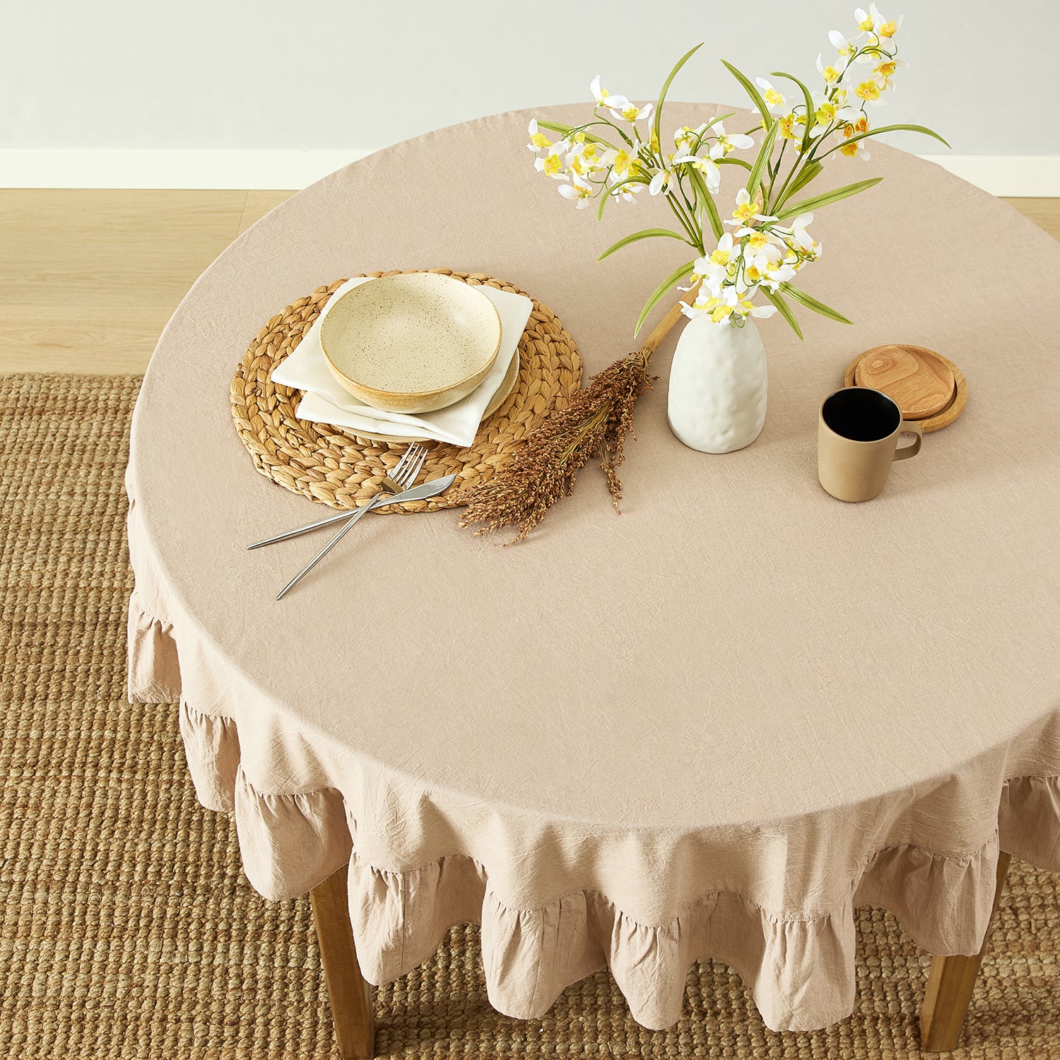 Round table with beige tablecloth, decorative items, and flowers on a wooden floor.