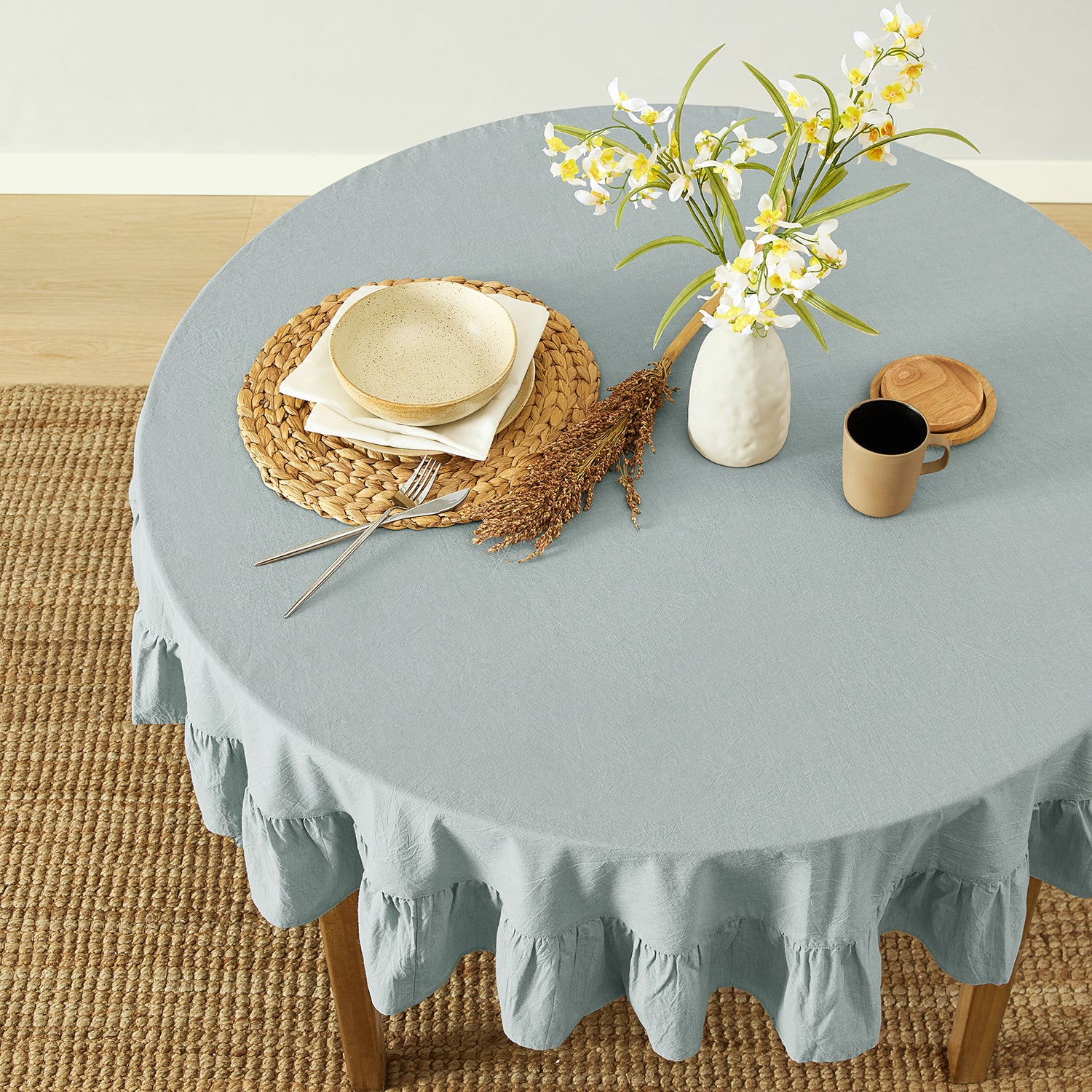 Round table with a light blue tablecloth, wicker placemat, ceramic bowl, and decorative elements.