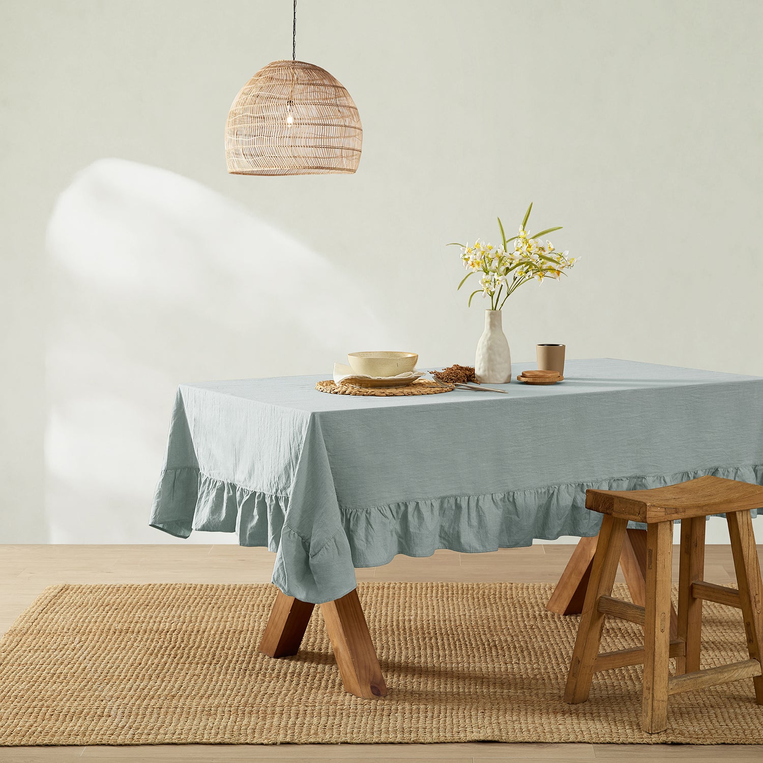 Dining table with a light blue tablecloth, wooden stool, and decorative elements in a room.
