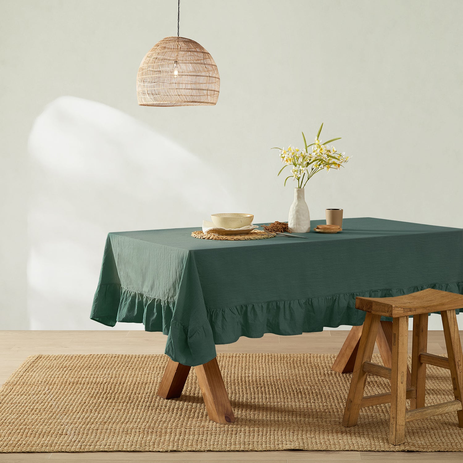 Green tablecloth on a dining table with a vase of flowers and a wooden stool.
