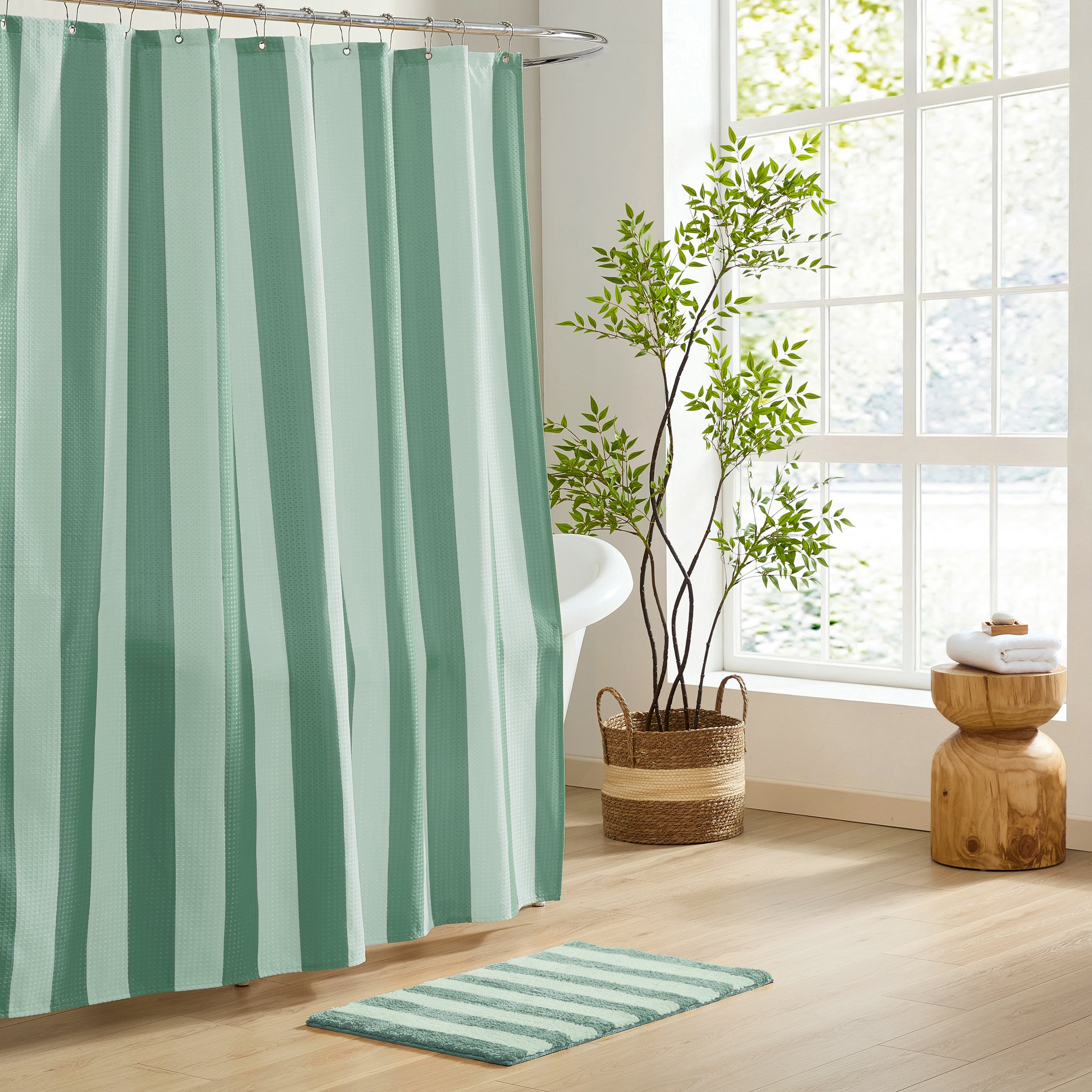 Bathroom with green and white striped shower curtain and rug, plant, and wooden stool.