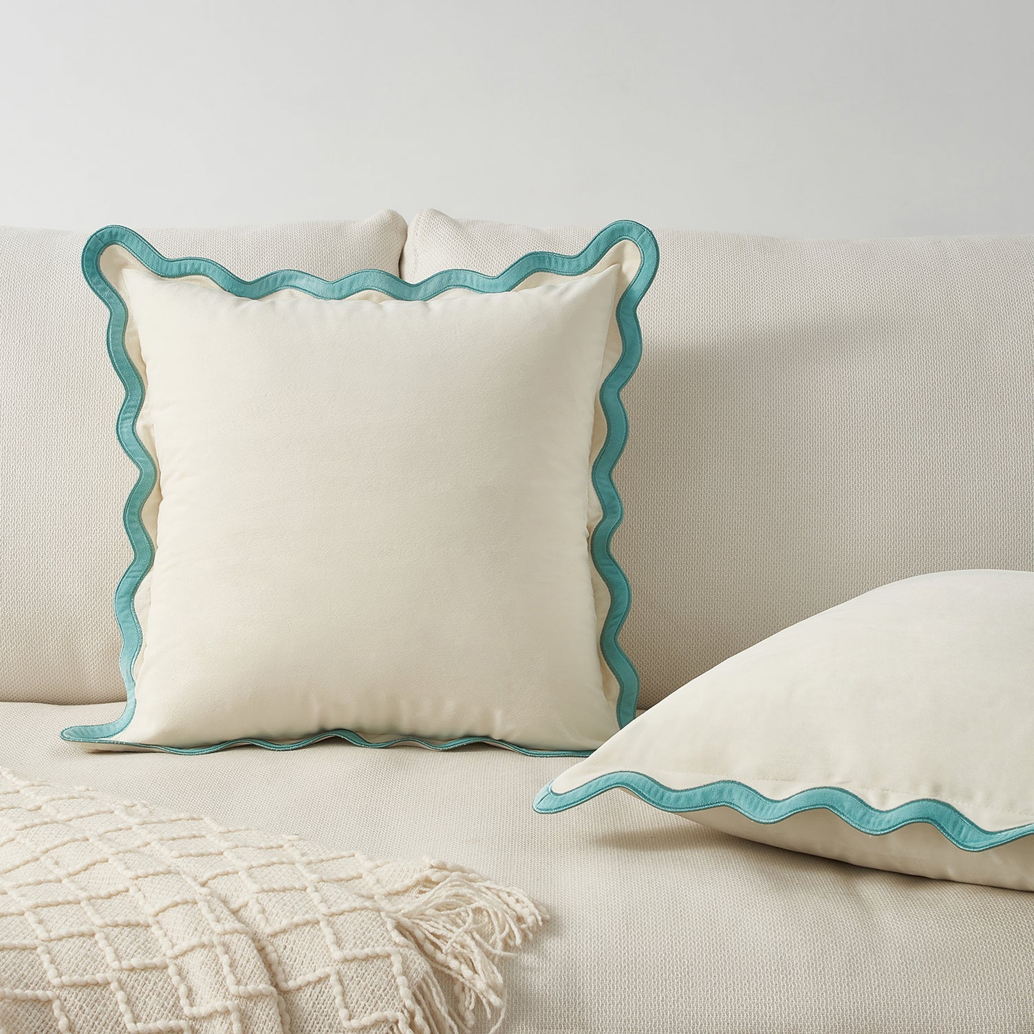Two decorative pillows with wavy blue edges on a beige sofa.