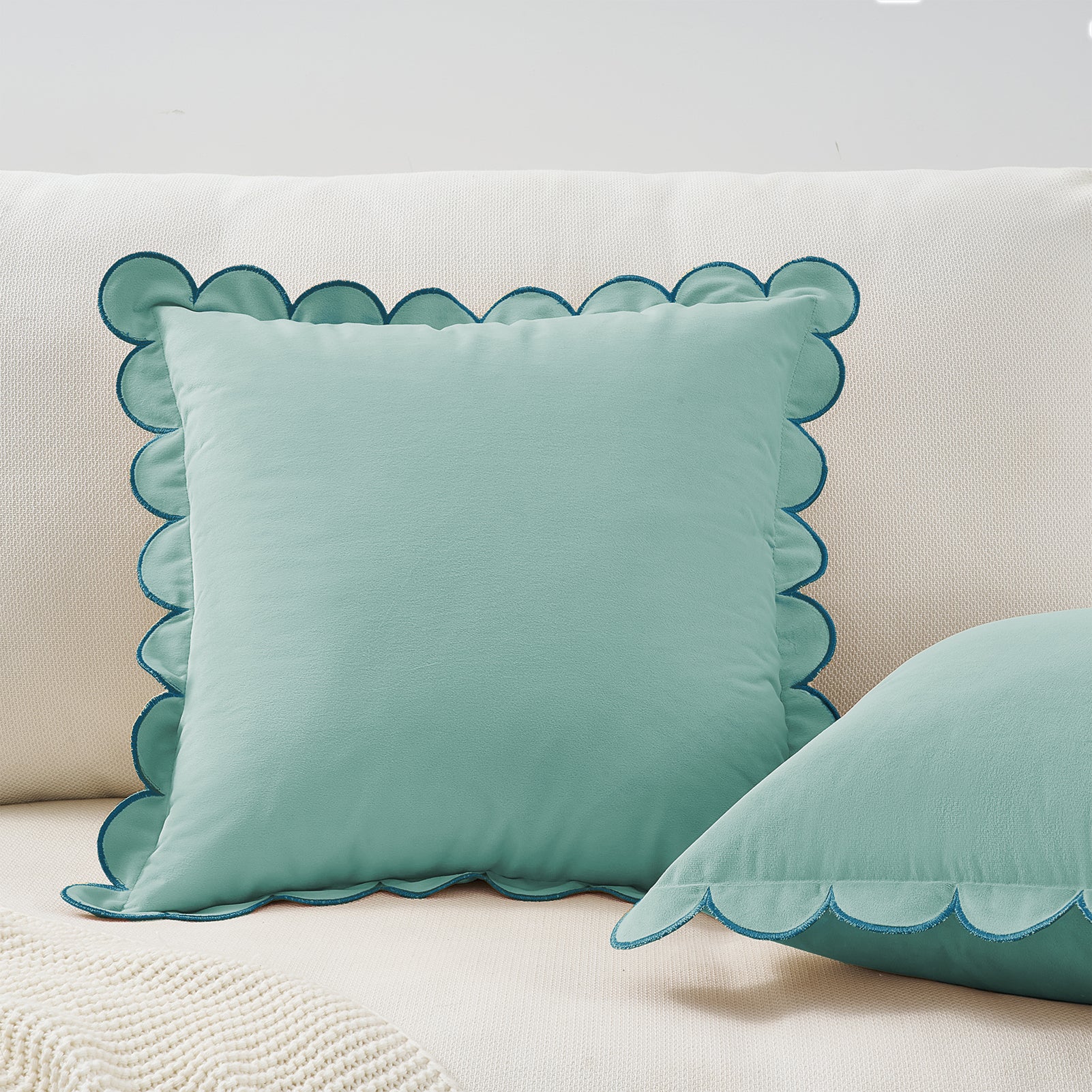 Teal pillow with scalloped edge on a beige sofa
