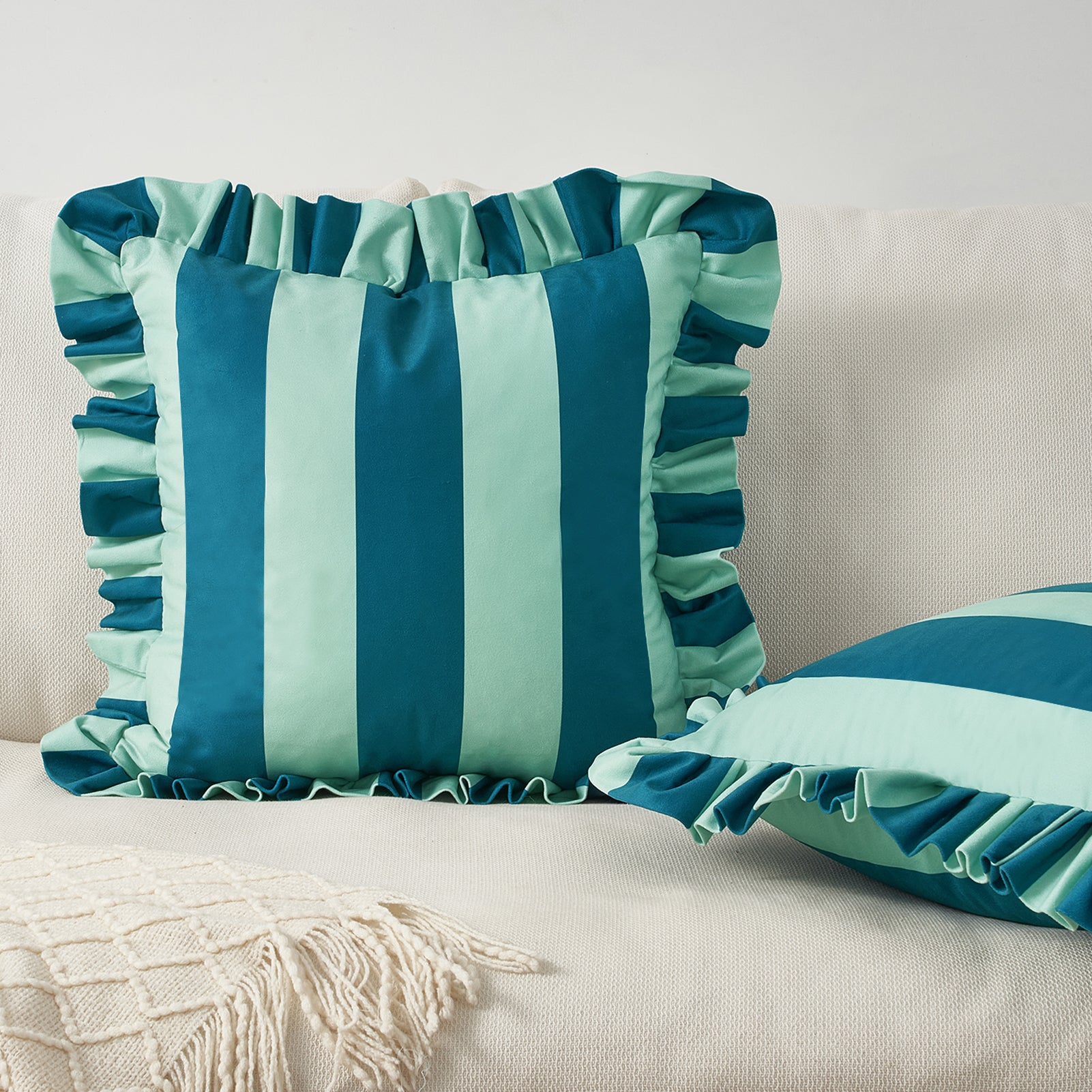 Teal and light blue striped pillows with ruffled edges on a beige couch.