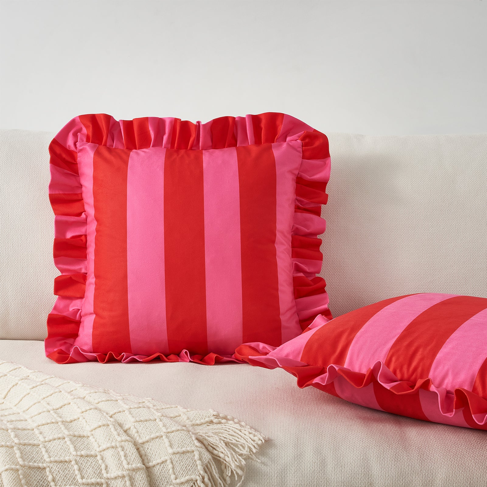 Two red and pink striped pillows on a beige couch.