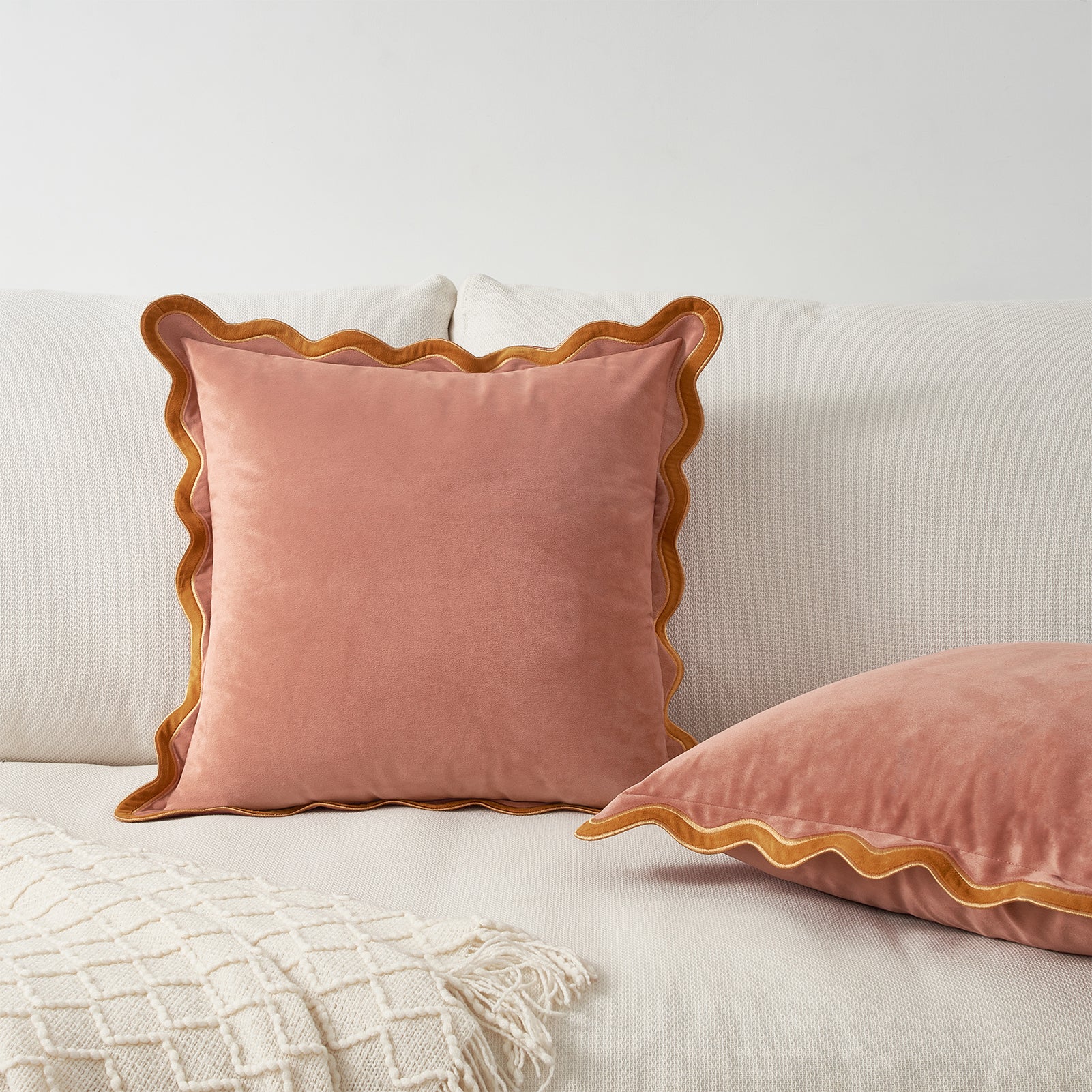 Pink velvet pillows with scalloped edges on a light-colored sofa.
