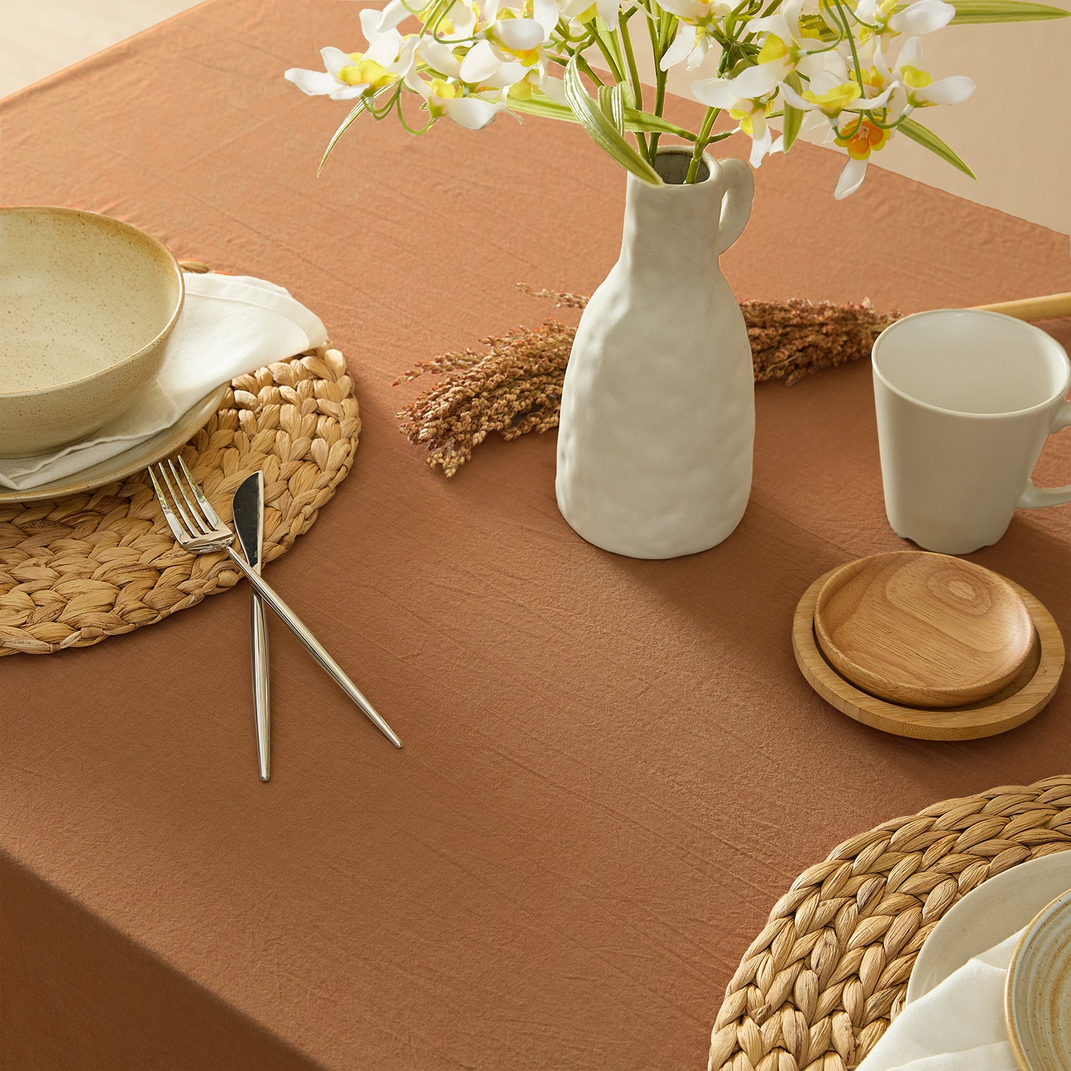 Table setting with a vase, mug, and plates on a brown tablecloth.