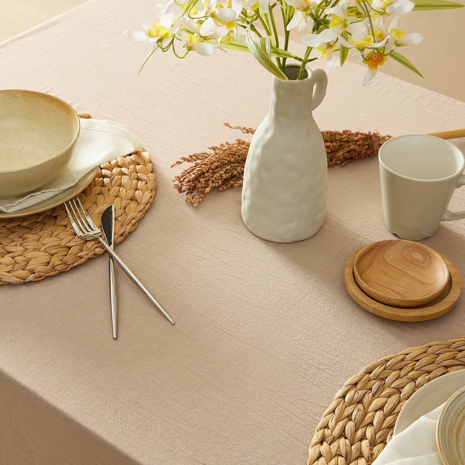 Table setting with ceramic plates, mug, and vase on a beige tablecloth.