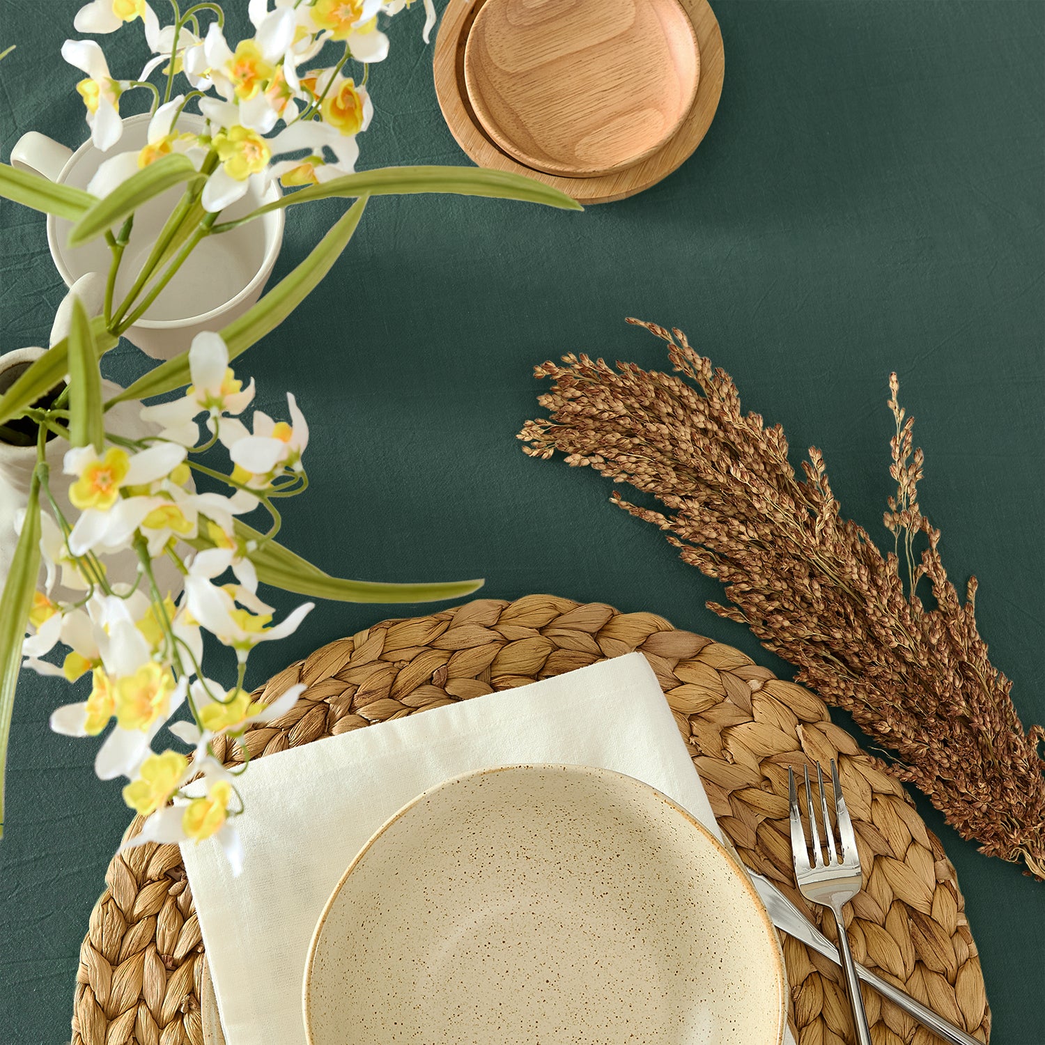 Table setting with ceramic plate, woven placemat, and decorative elements on a dark green surface.