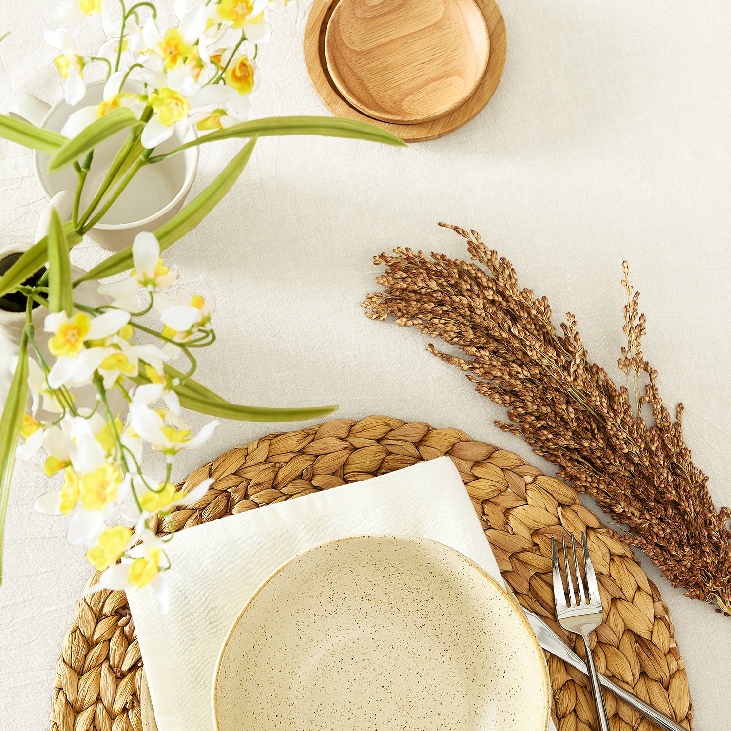 Table setting with ceramic plate, wooden coaster, and decorative elements on a white surface.