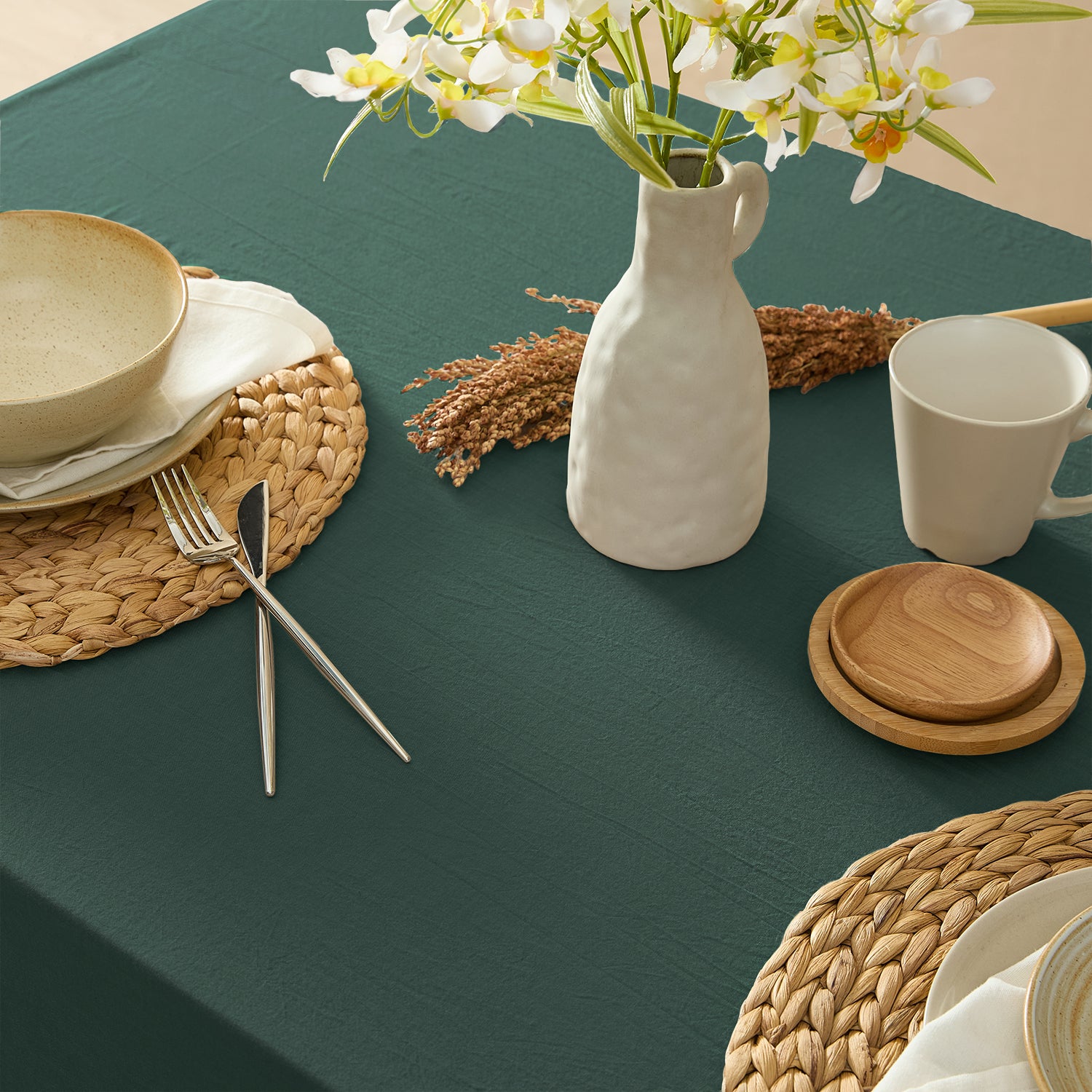 Table setting with a vase, mug, and cutlery on a green tablecloth.