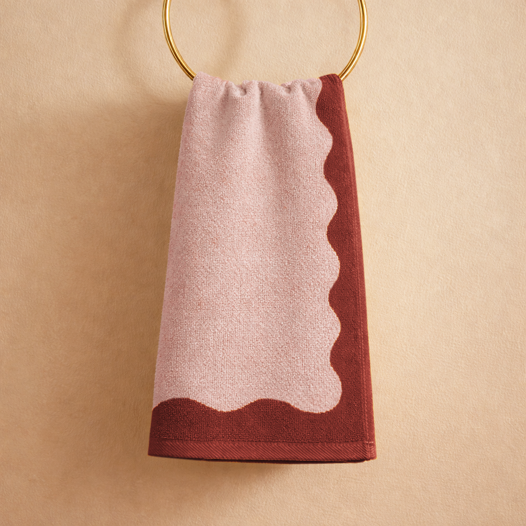 Towel with scalloped edge hanging on a gold ring against a beige background