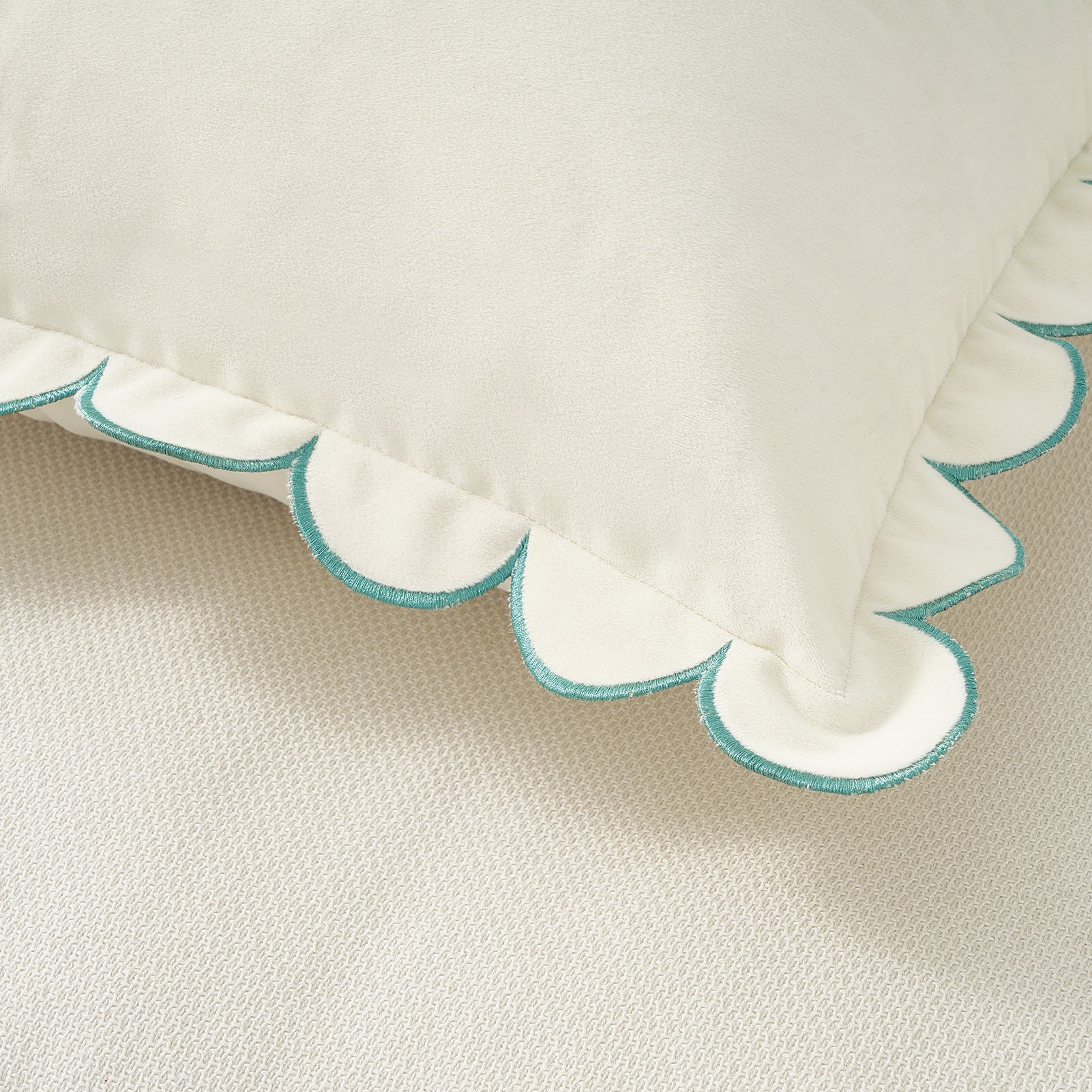 Close-up of a pillow with scalloped edge and turquoise trim on a beige background