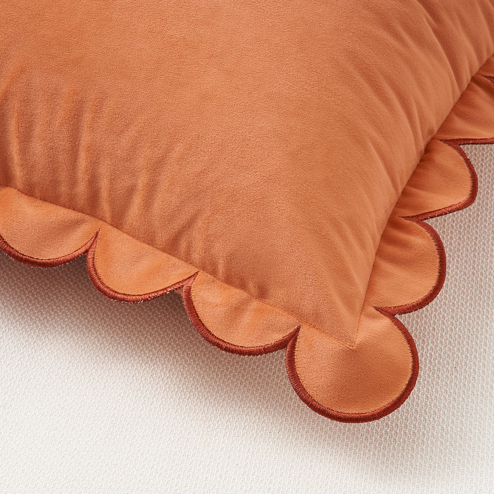 Orange pillow with scalloped edge on a beige background