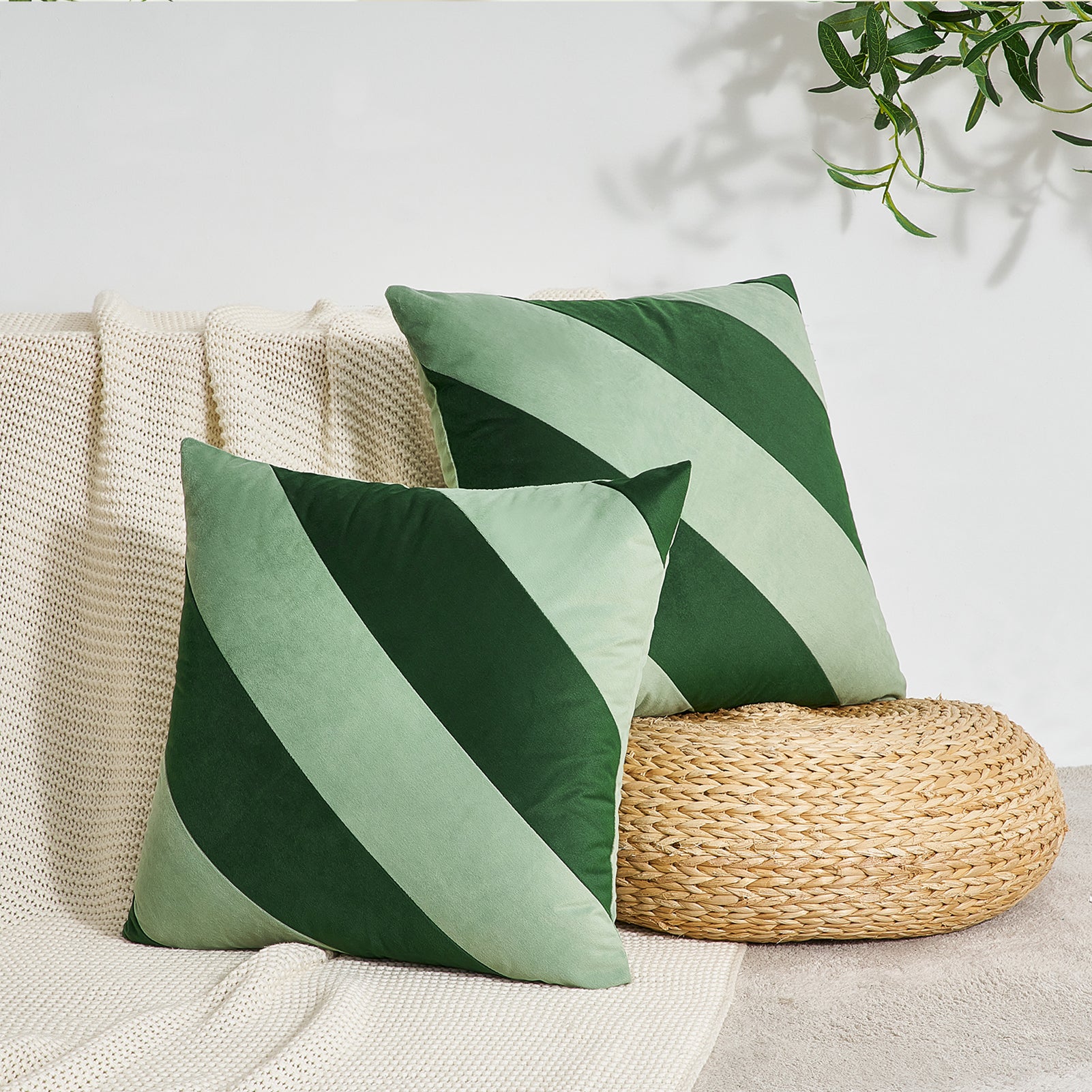 Green and white striped pillows on a beige sofa with a woven footstool.