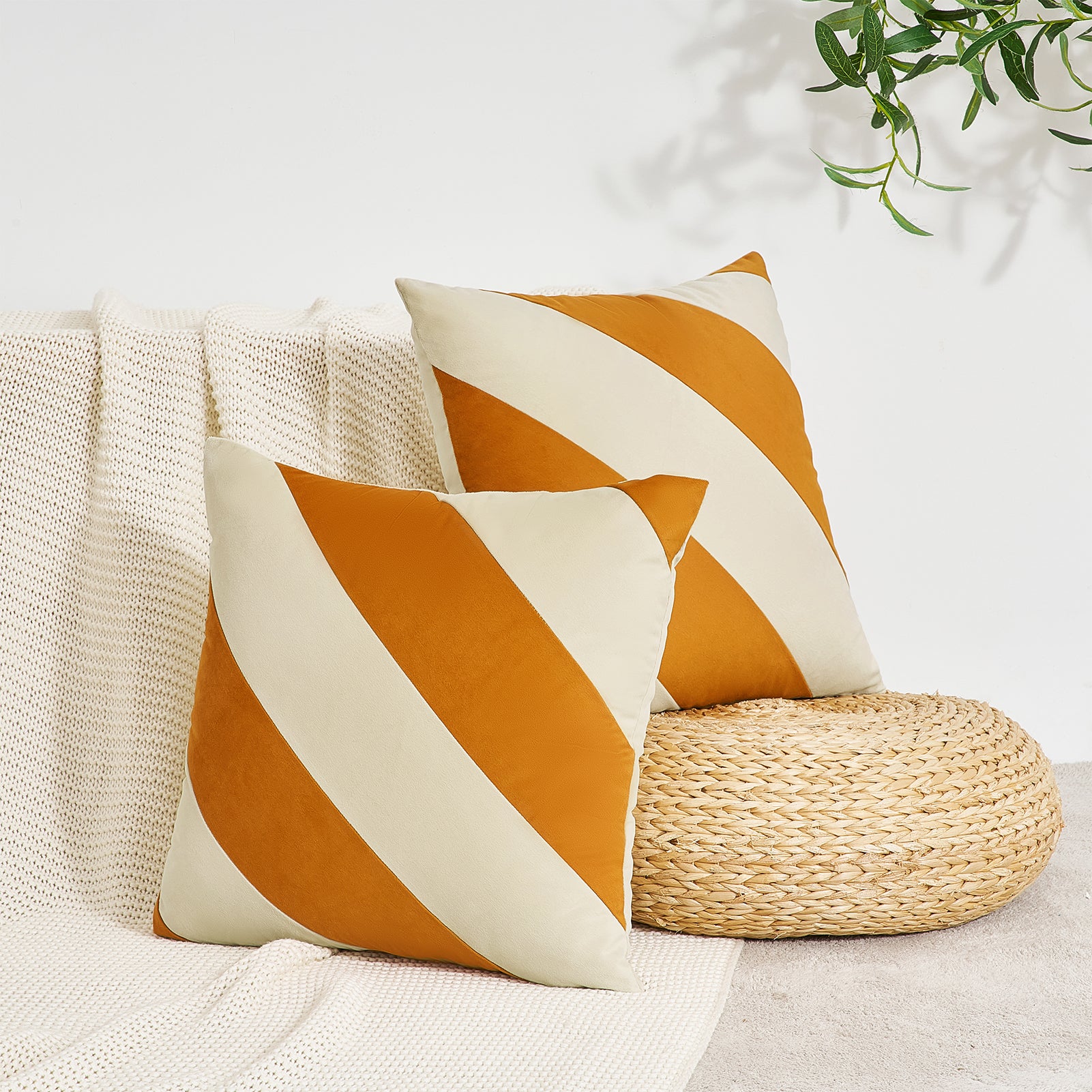 Two orange and white striped pillows on a couch with a plant in the background.