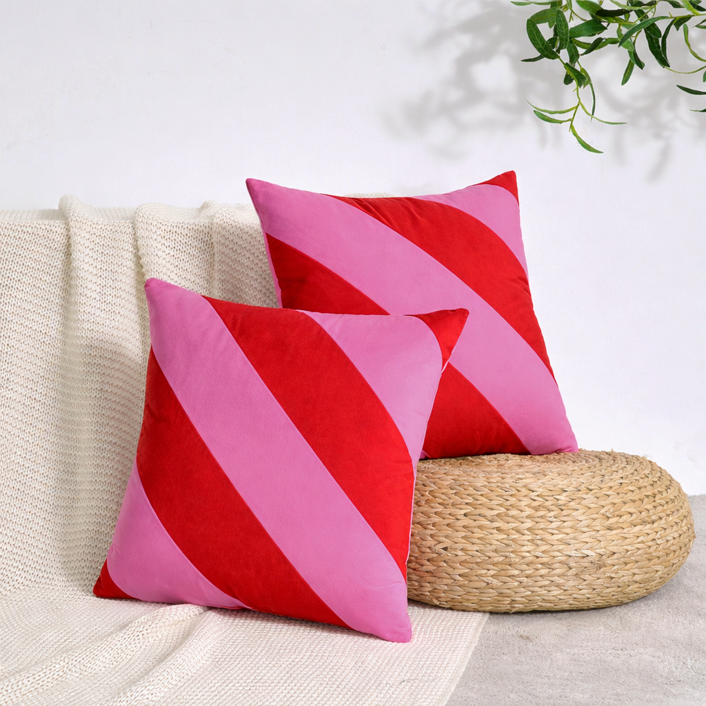 Two red and pink striped pillows on a beige couch with a plant in the background.