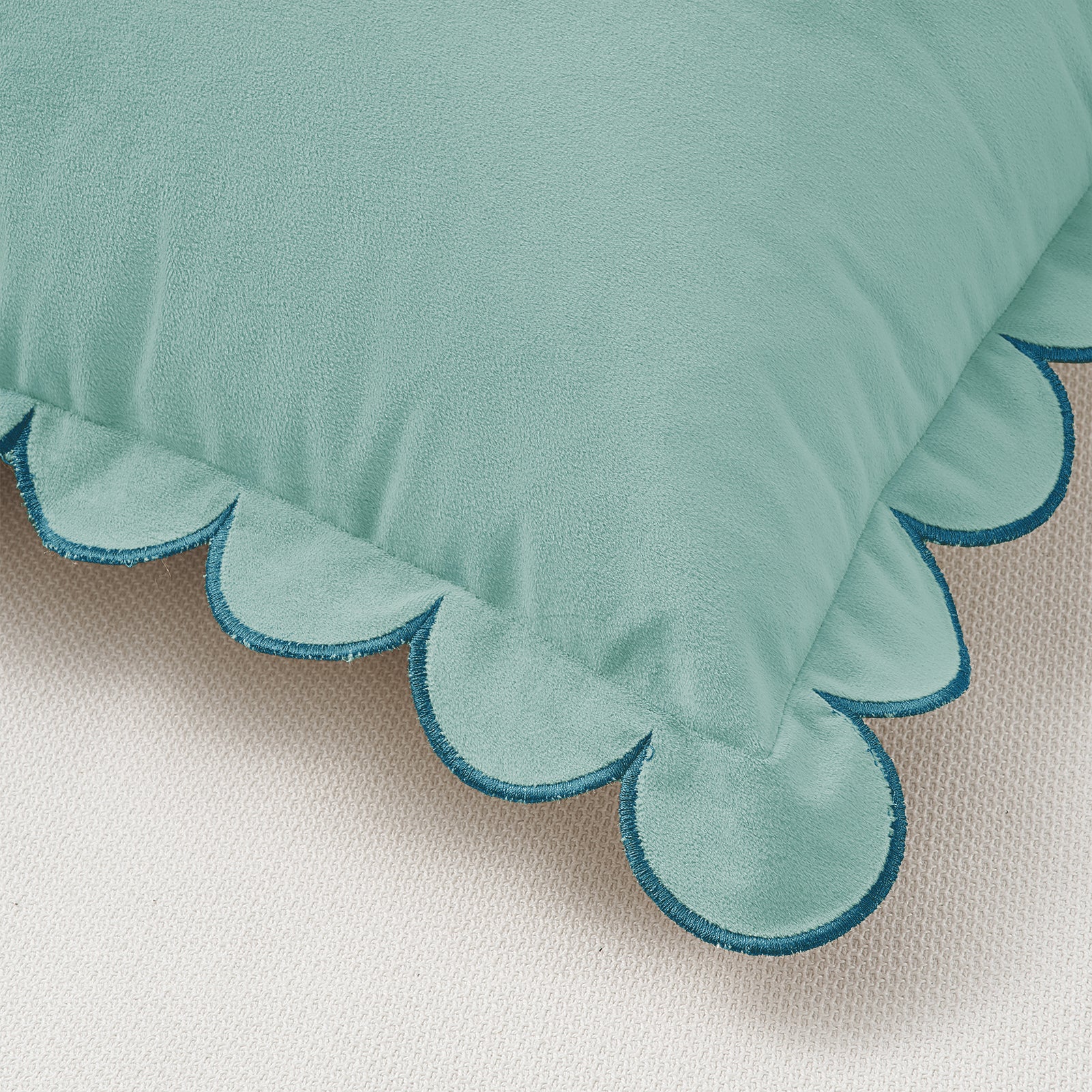Teal pillow with scalloped edge on a beige background