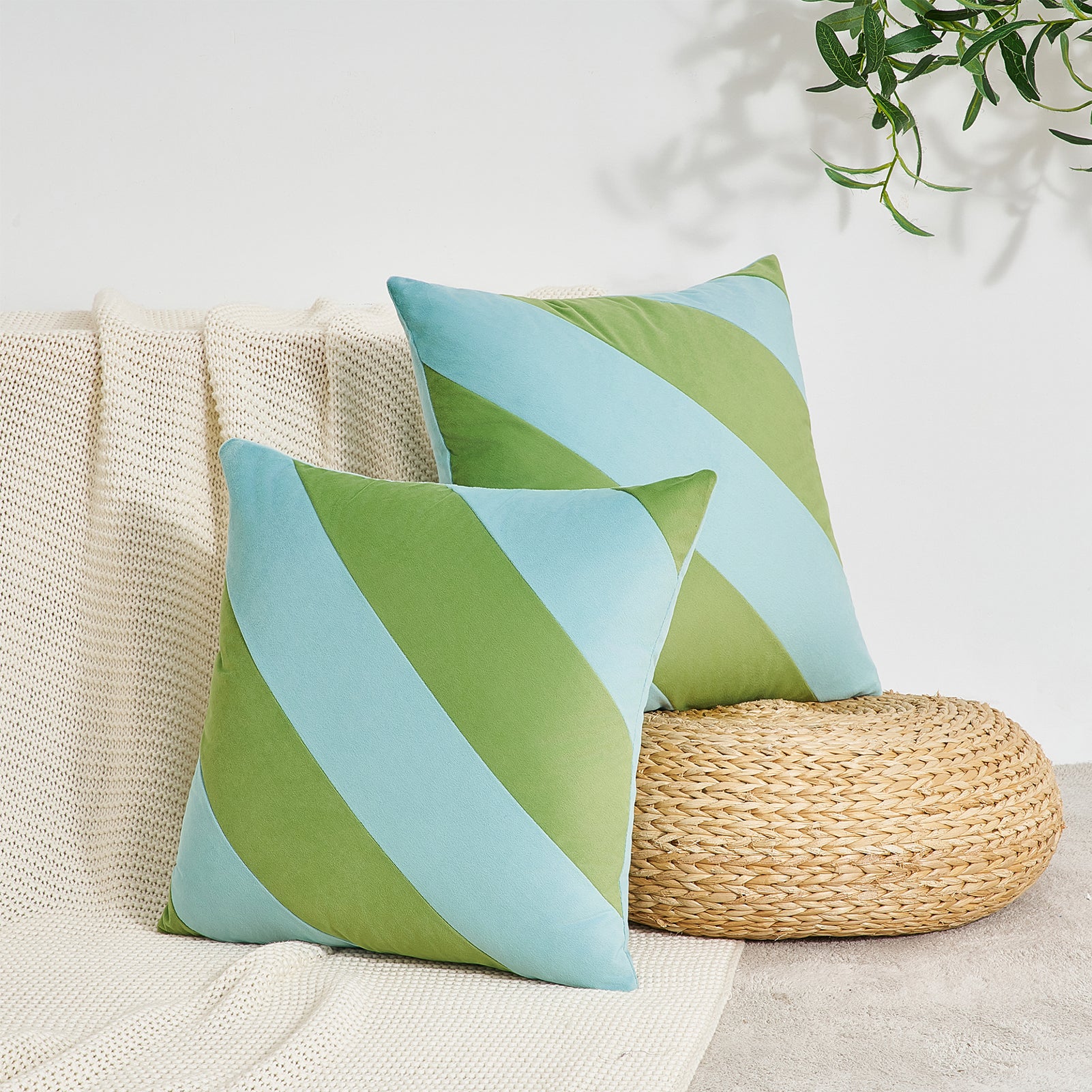 Two green and blue striped pillows on a beige couch with a woven ottoman and plant in the background.