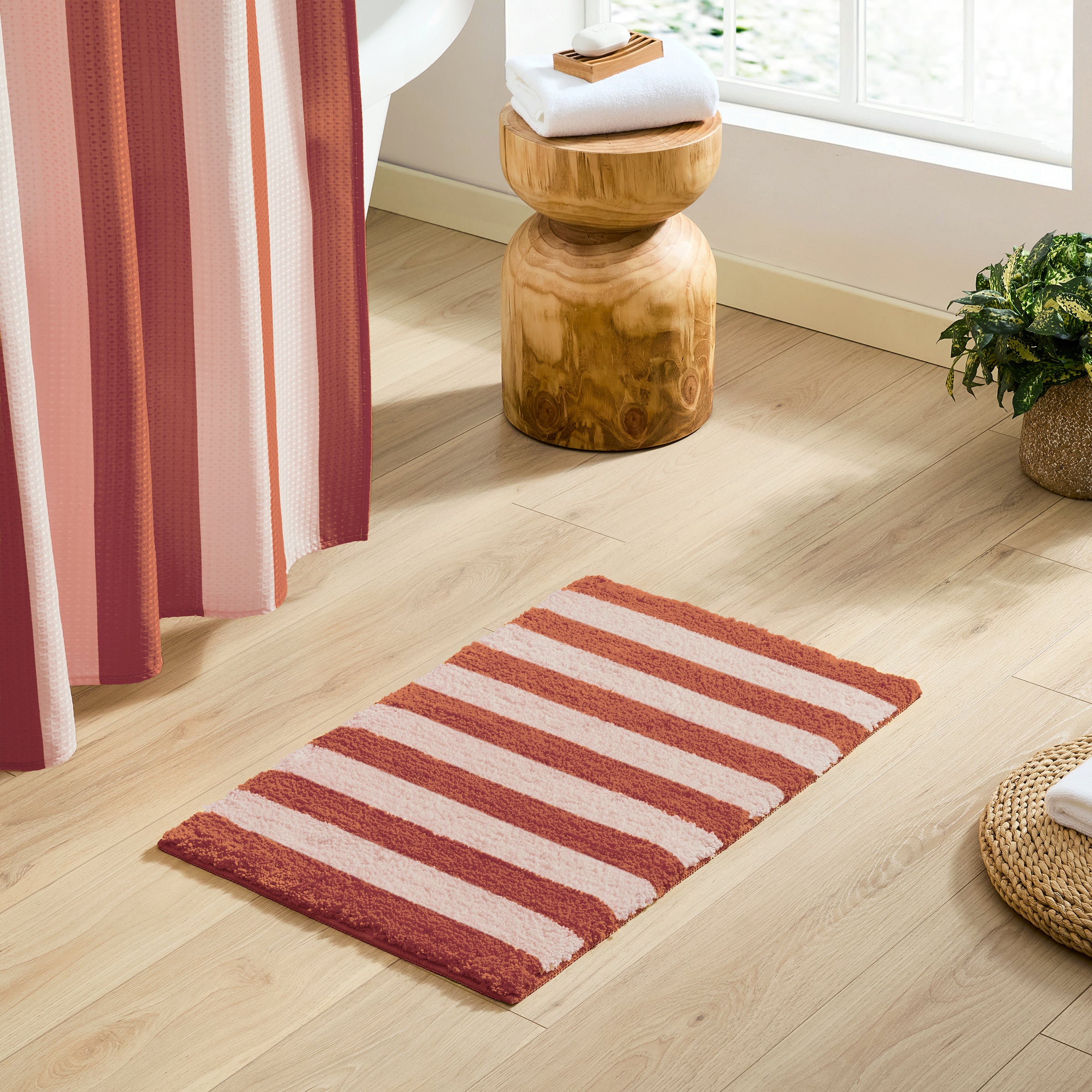 Striped red and beige rug on a wooden floor with a wooden side table and striped curtains.