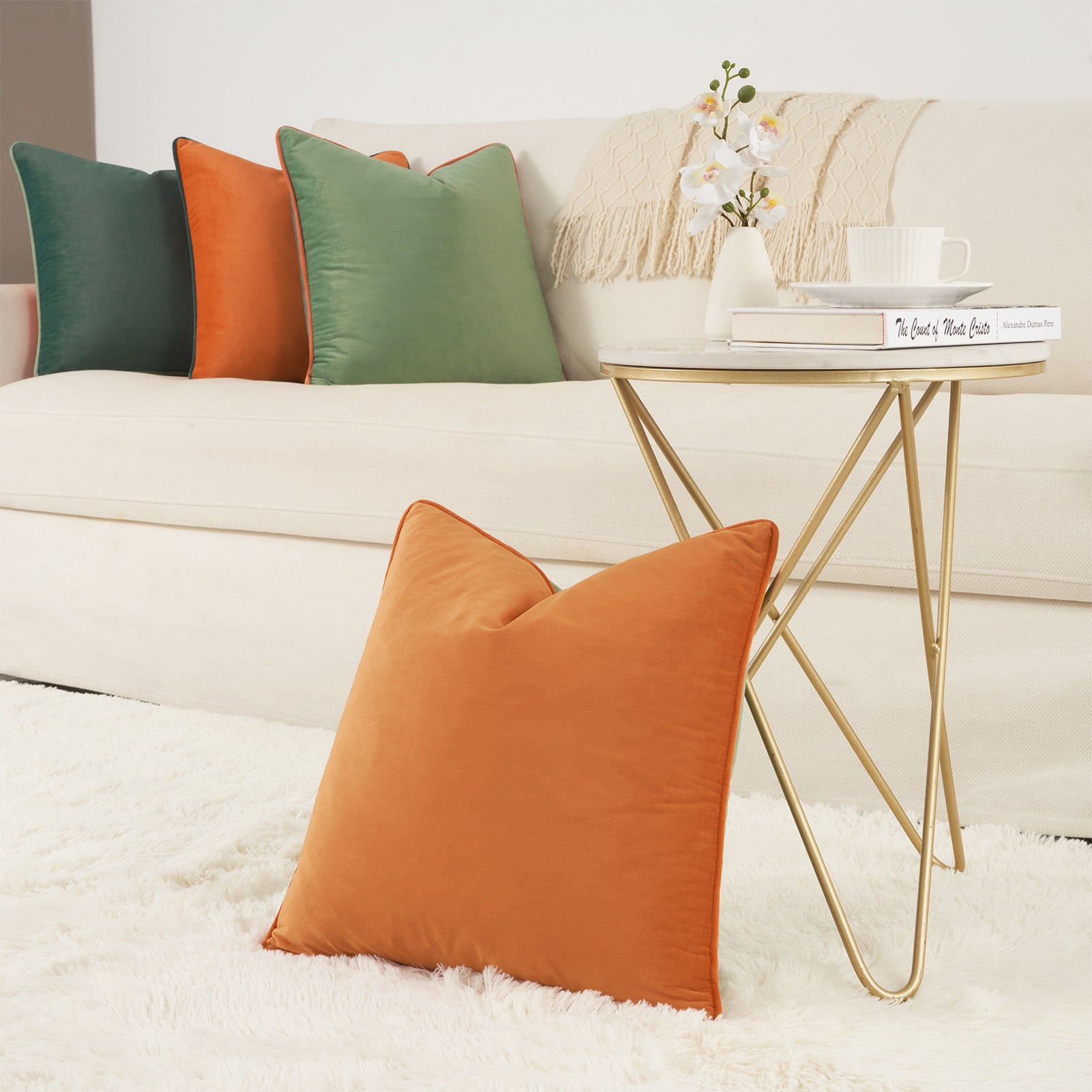Orange pillow on a white sofa with a gold side table and decorative items.