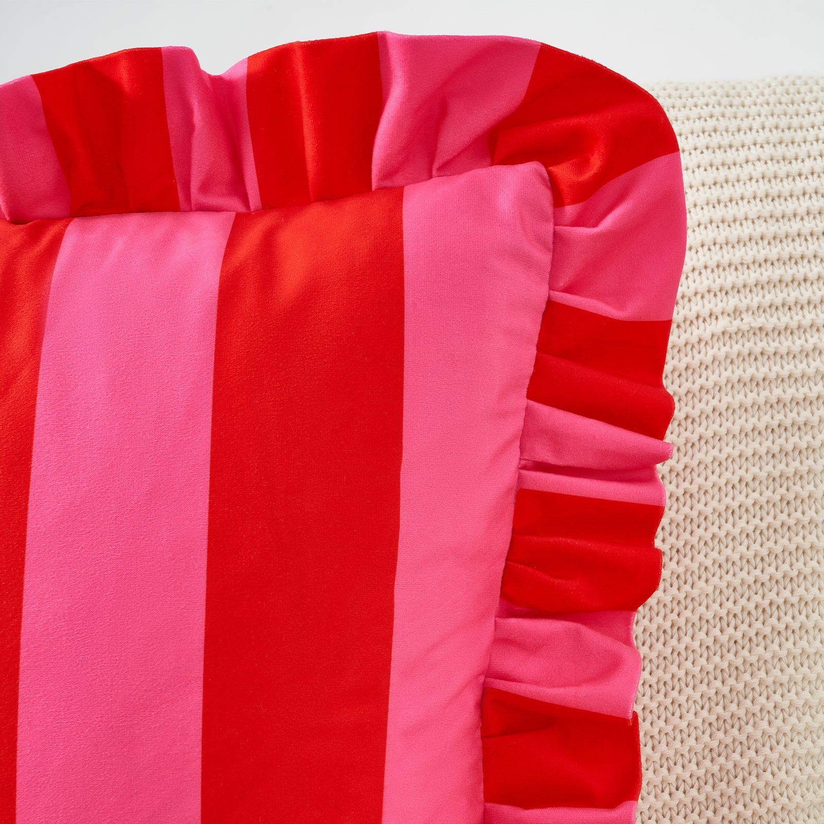 Red and pink striped pillow with ruffled edge on a textured surface