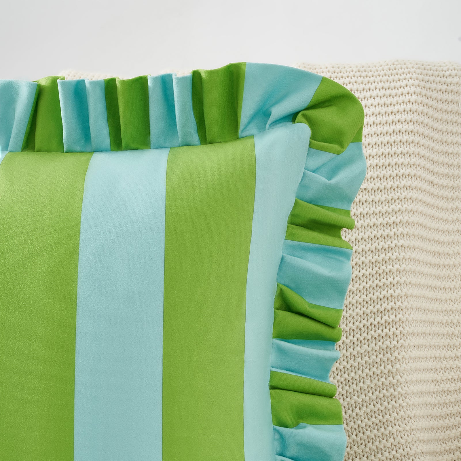 Close-up of a green and blue striped fabric with ruffled edges on a textured beige background.