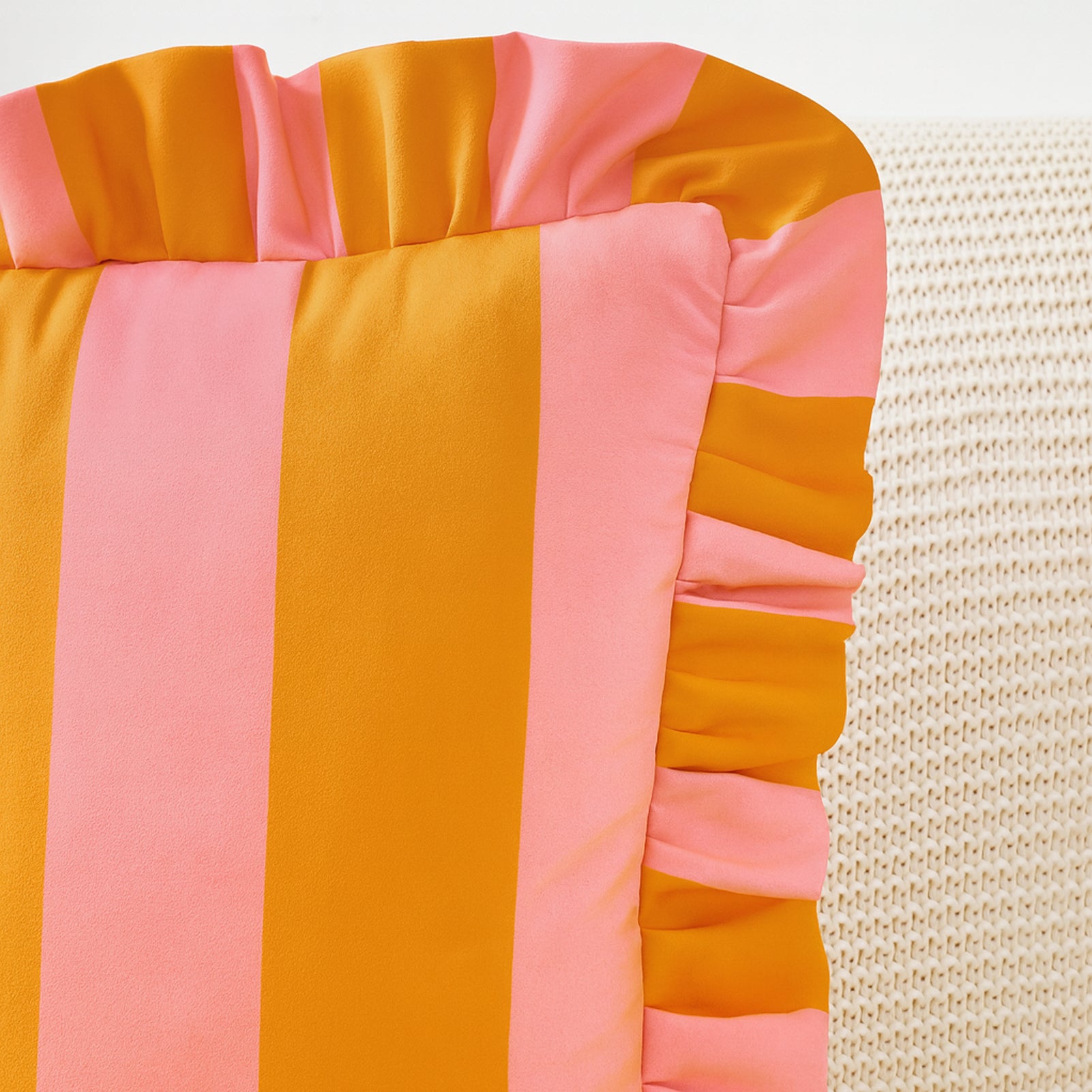 Colorful striped cushion with pink and orange pattern on a textured beige background