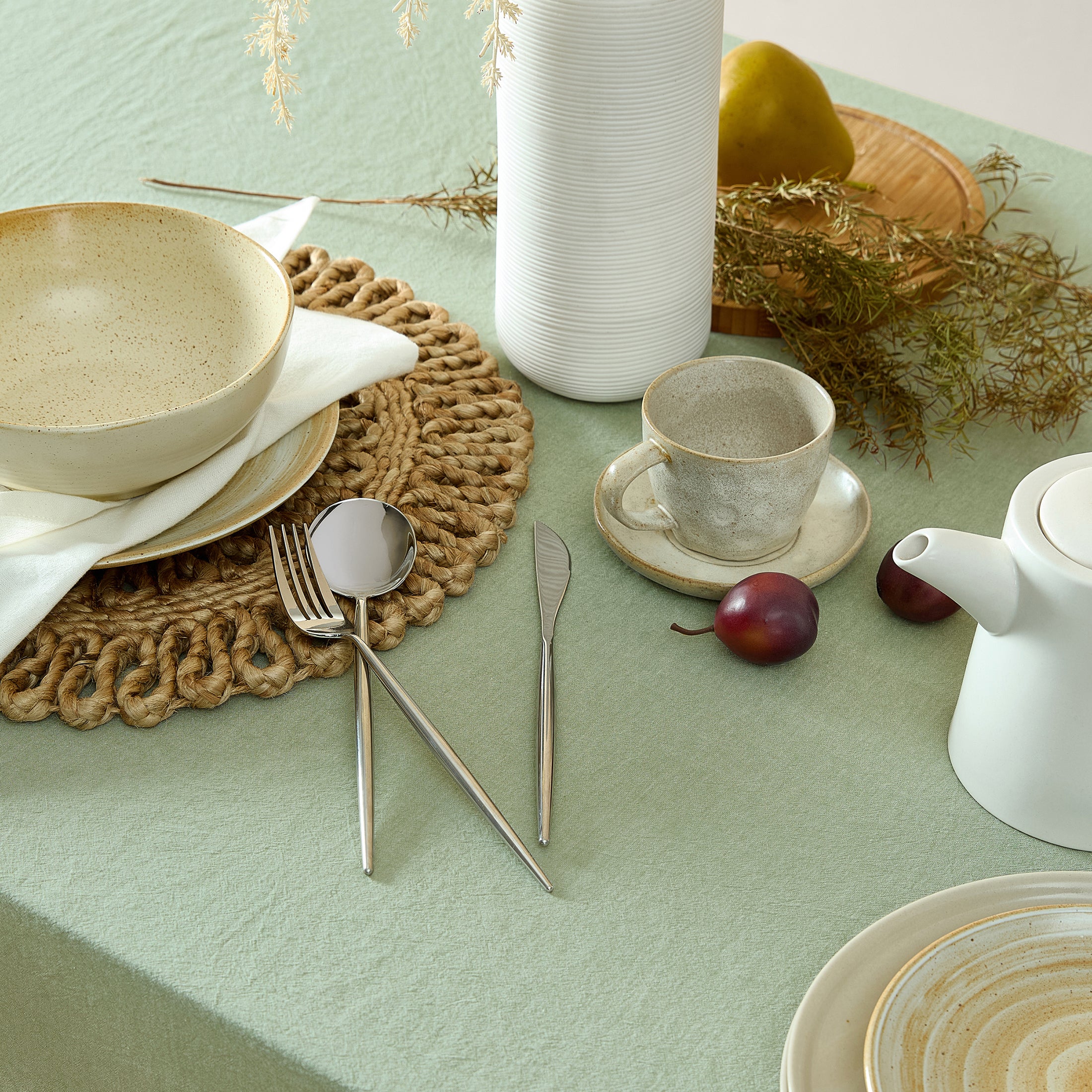 Table setting with ceramic bowls, teapot, and cutlery on a light green tablecloth.