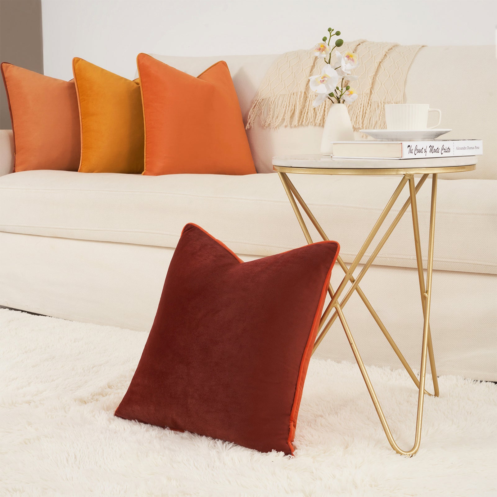 Decorative pillows on a sofa with a gold side table and books in a living room setting.