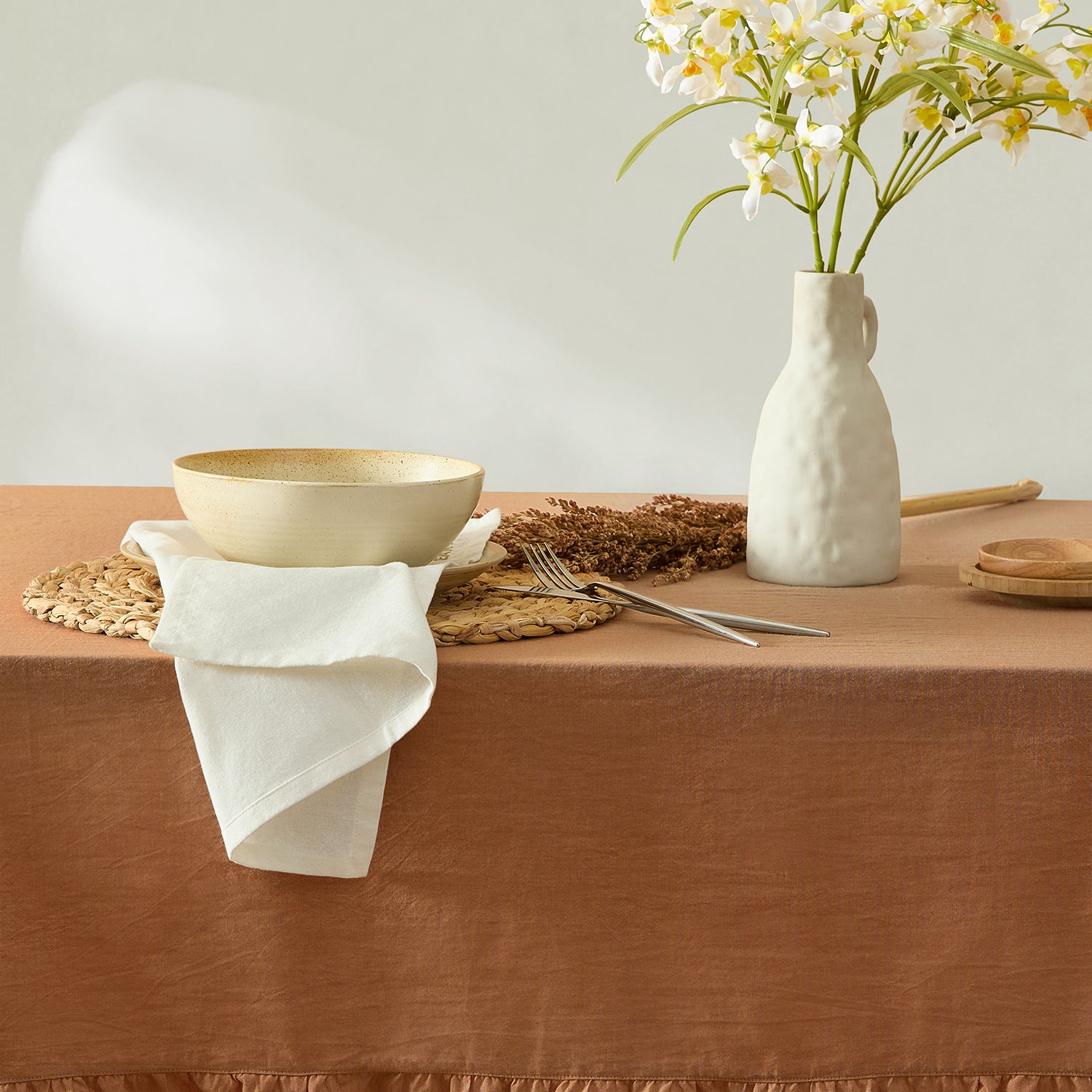 Table setting with a bowl, vase, and flowers on a brown tablecloth.
