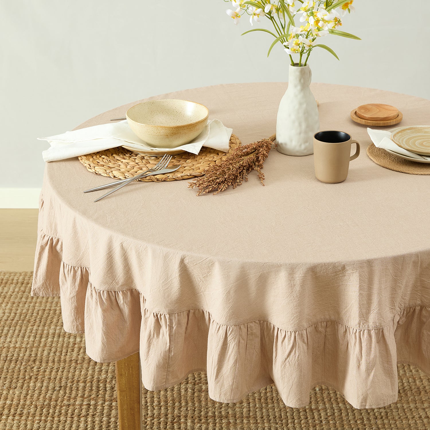 Round table with beige tablecloth, plates, mug, and vase on a light background