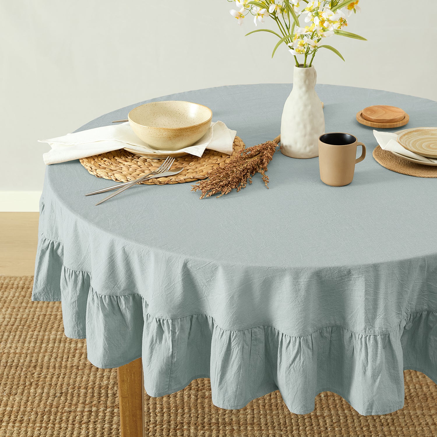 Round table with a light blue tablecloth, plates, cups, and a vase with flowers on a neutral background.