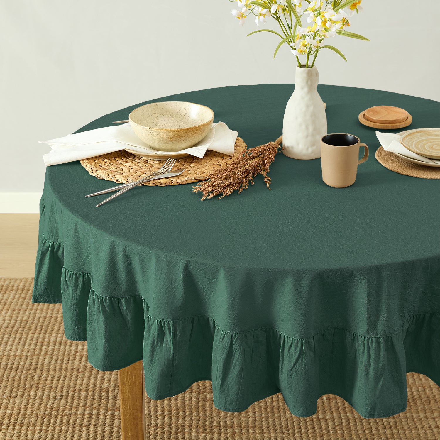 Round table with a green tablecloth, plates, cups, and a vase with flowers on a beige carpet.