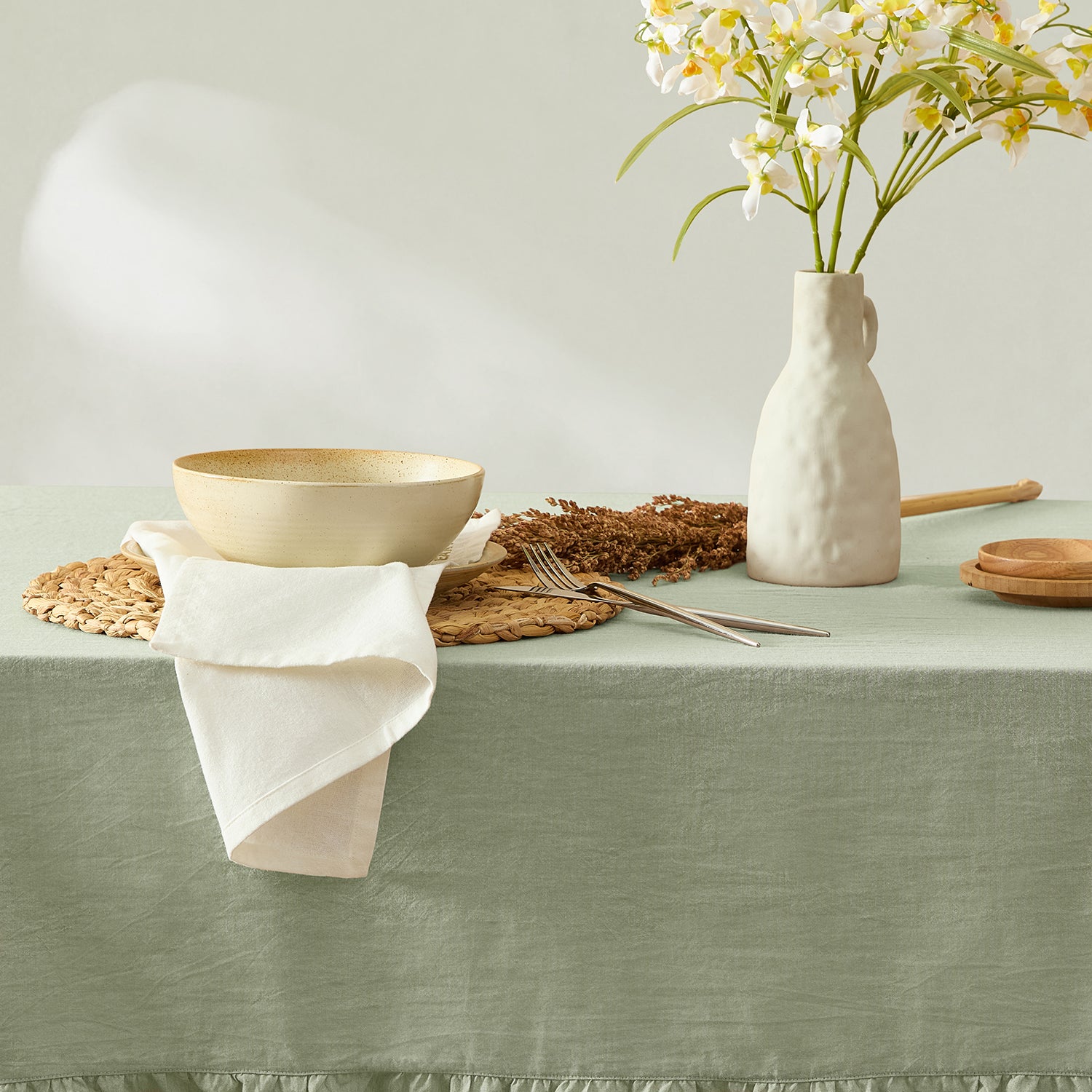 Table setting with a vase of flowers, bowls, and cutlery on a green tablecloth.