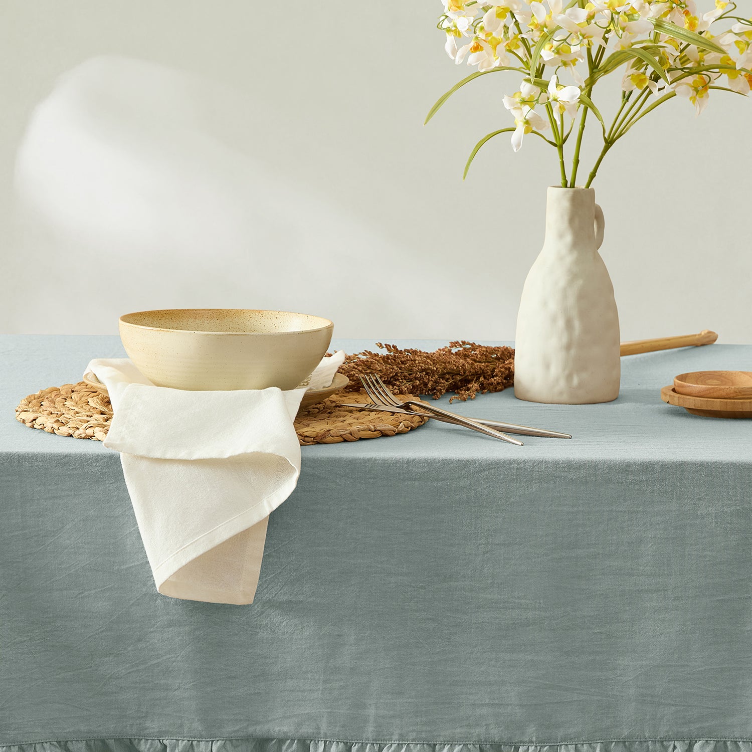 Table setting with a bowl, vase, and flowers on a gray tablecloth.