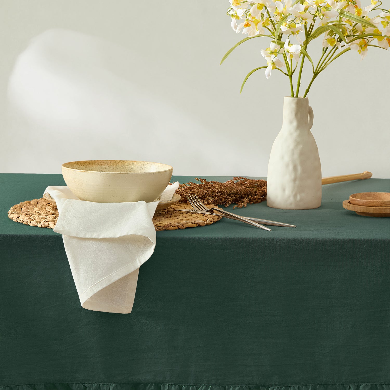 Table setting with a bowl, vase, and flowers on a green tablecloth.