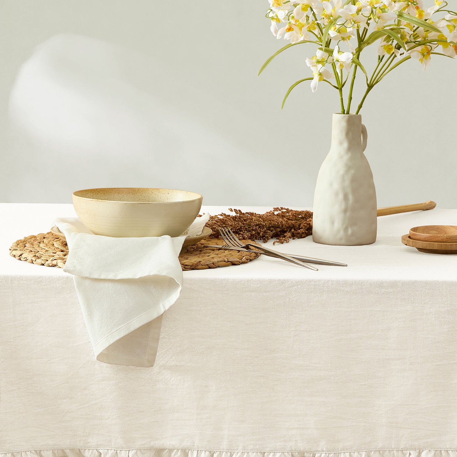Table setting with a bowl, vase, and flowers on a white tablecloth.