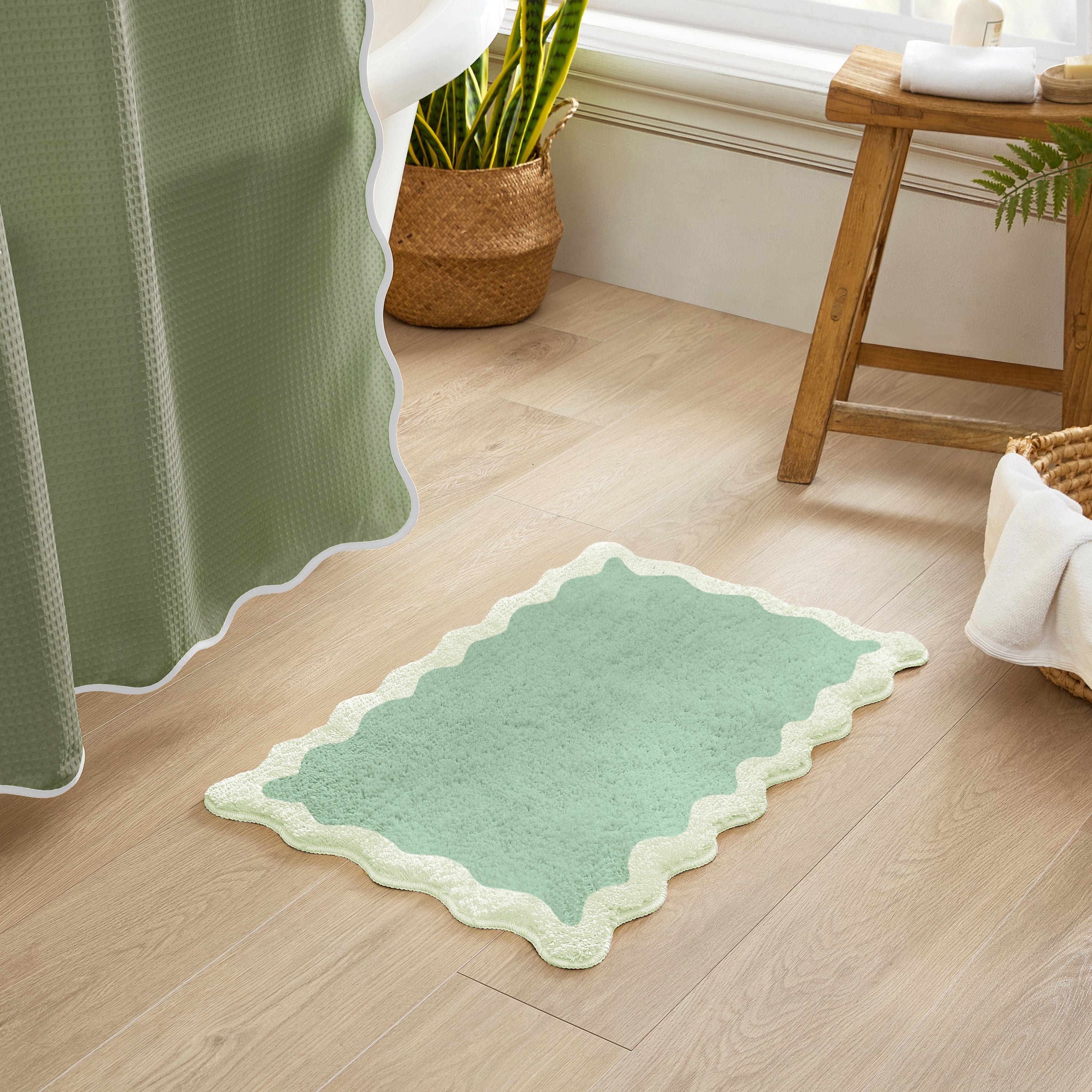 Green bath mat on a wooden floor with a curtain and plant in the background