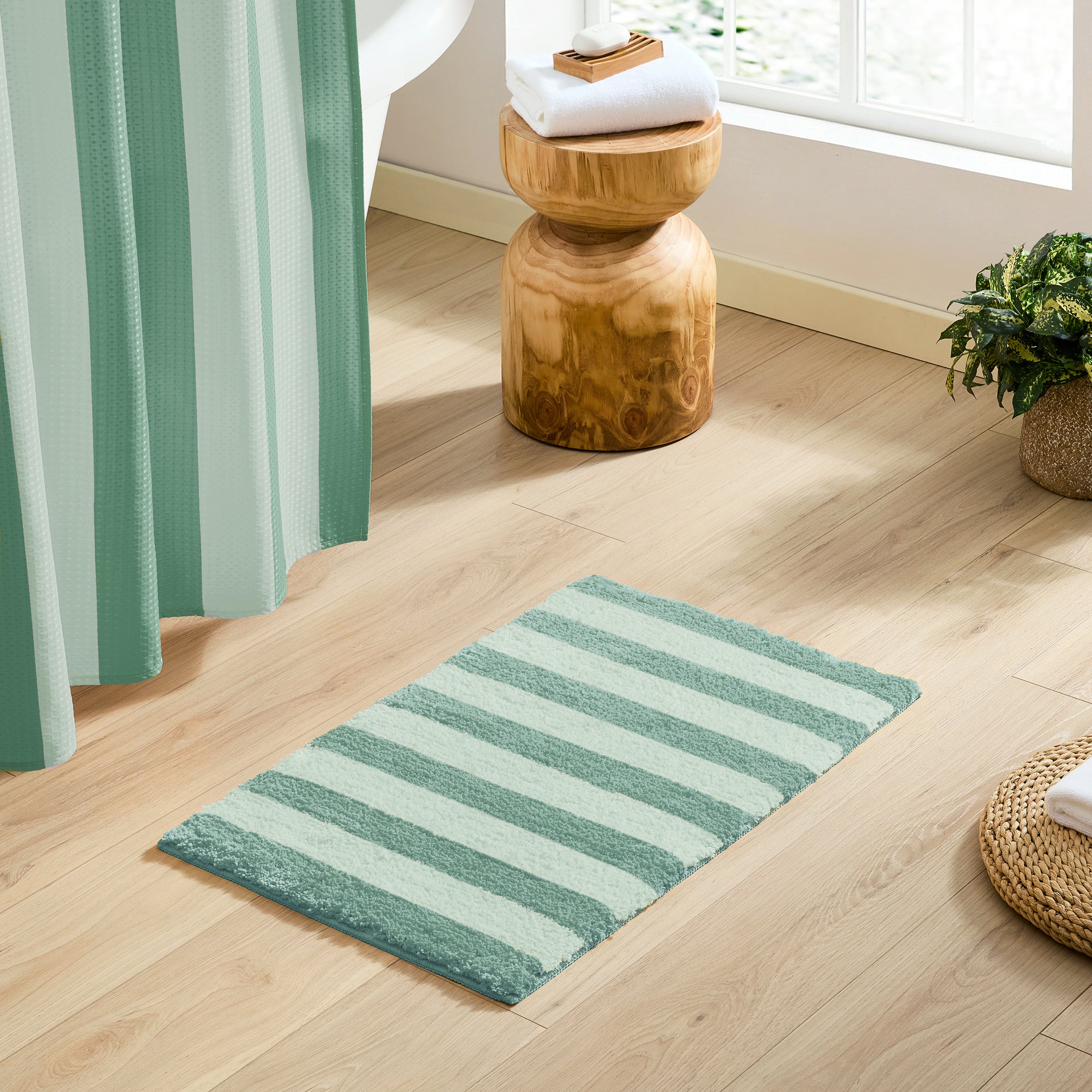 Green and white striped rug on a wooden floor with a wooden stool and plant in the background.