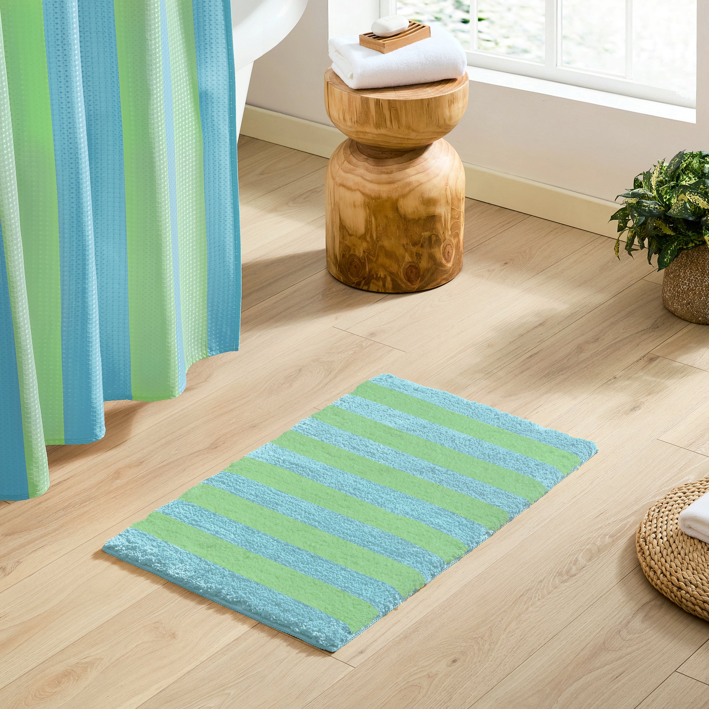Striped green and blue bath mat on a wooden floor with a curtain and stool in the background.