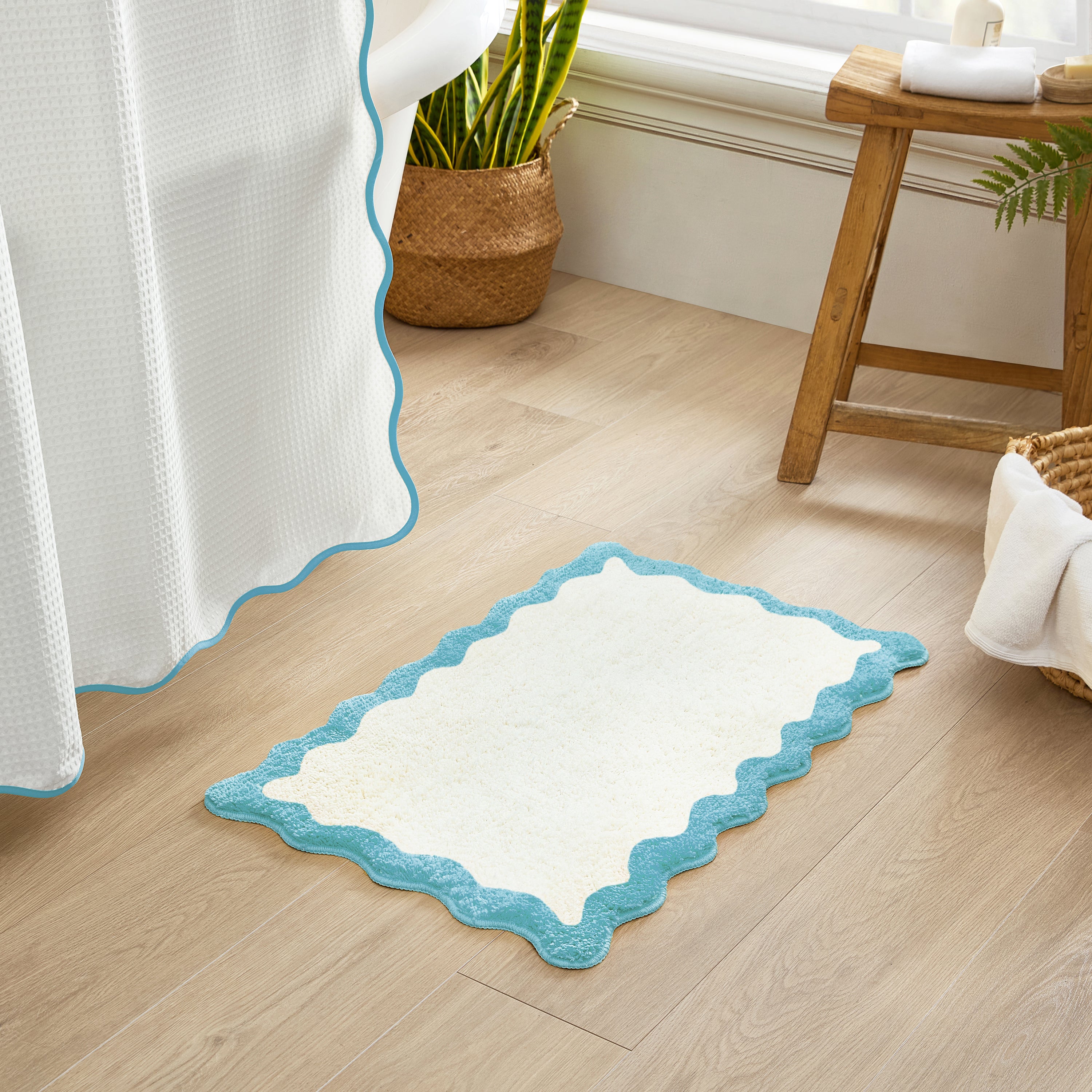 White bath mat with blue border on a wooden floor next to a window.