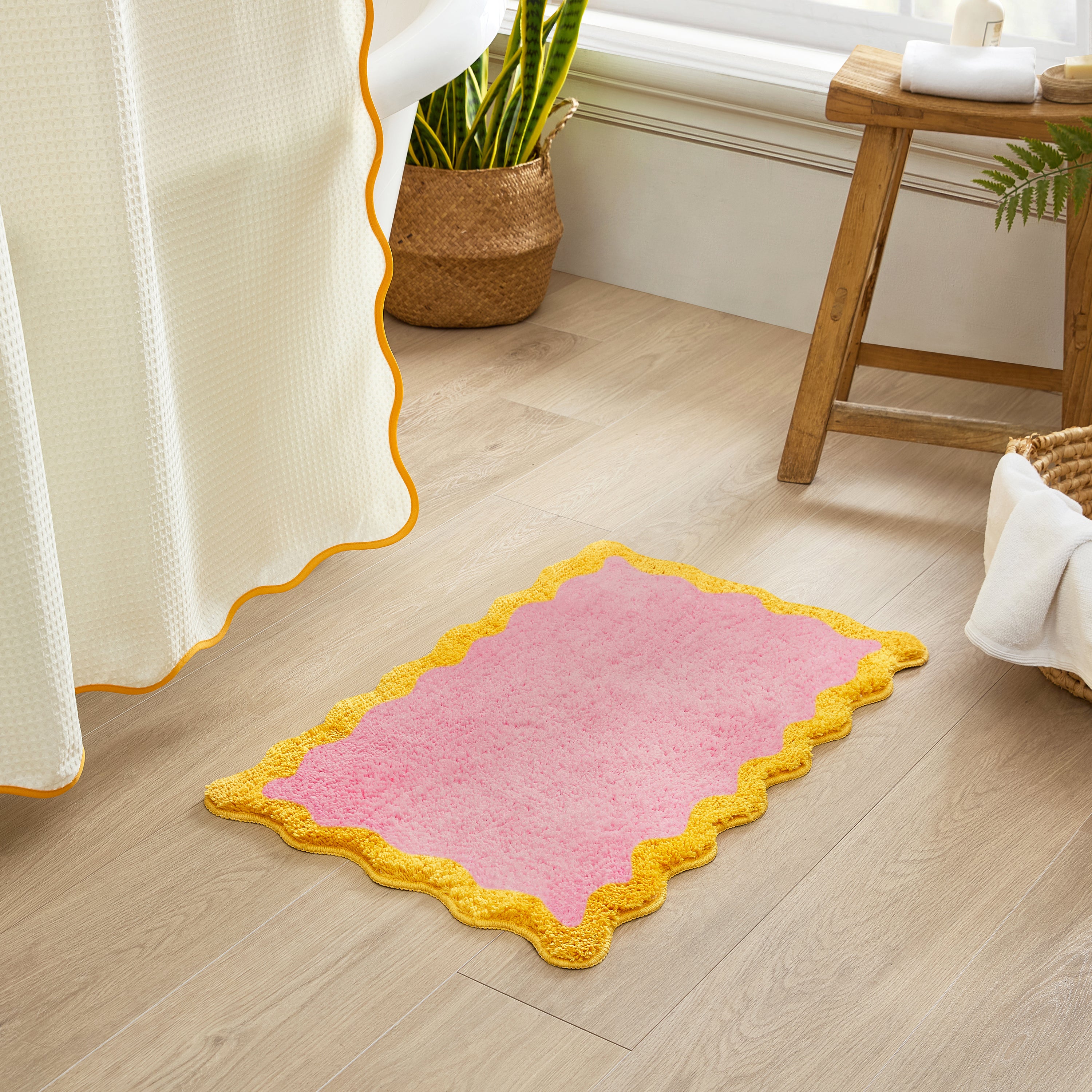 Pink rug with yellow border on a wooden floor next to a window.
