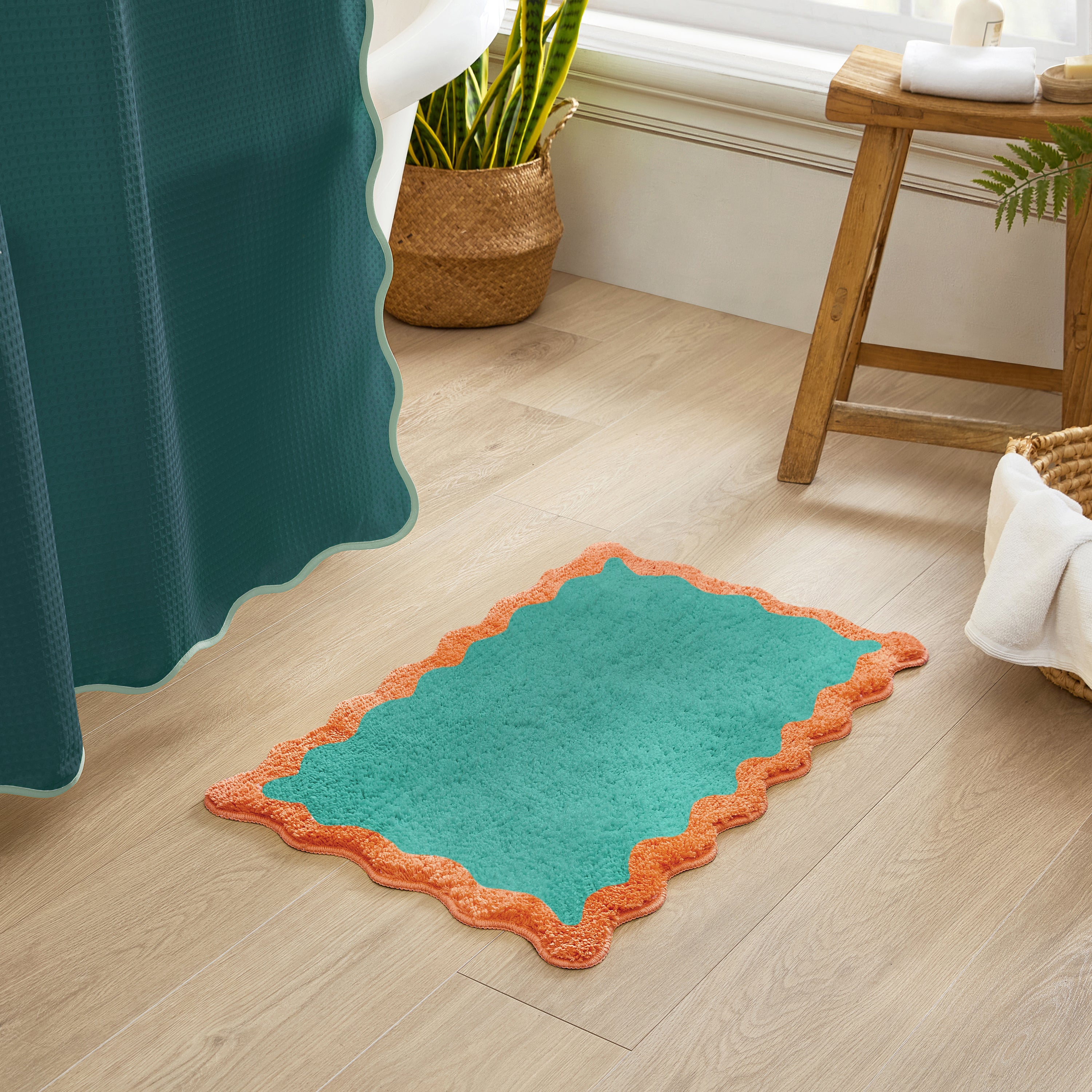 Teal bath mat with orange border on a wooden floor next to a shower curtain.