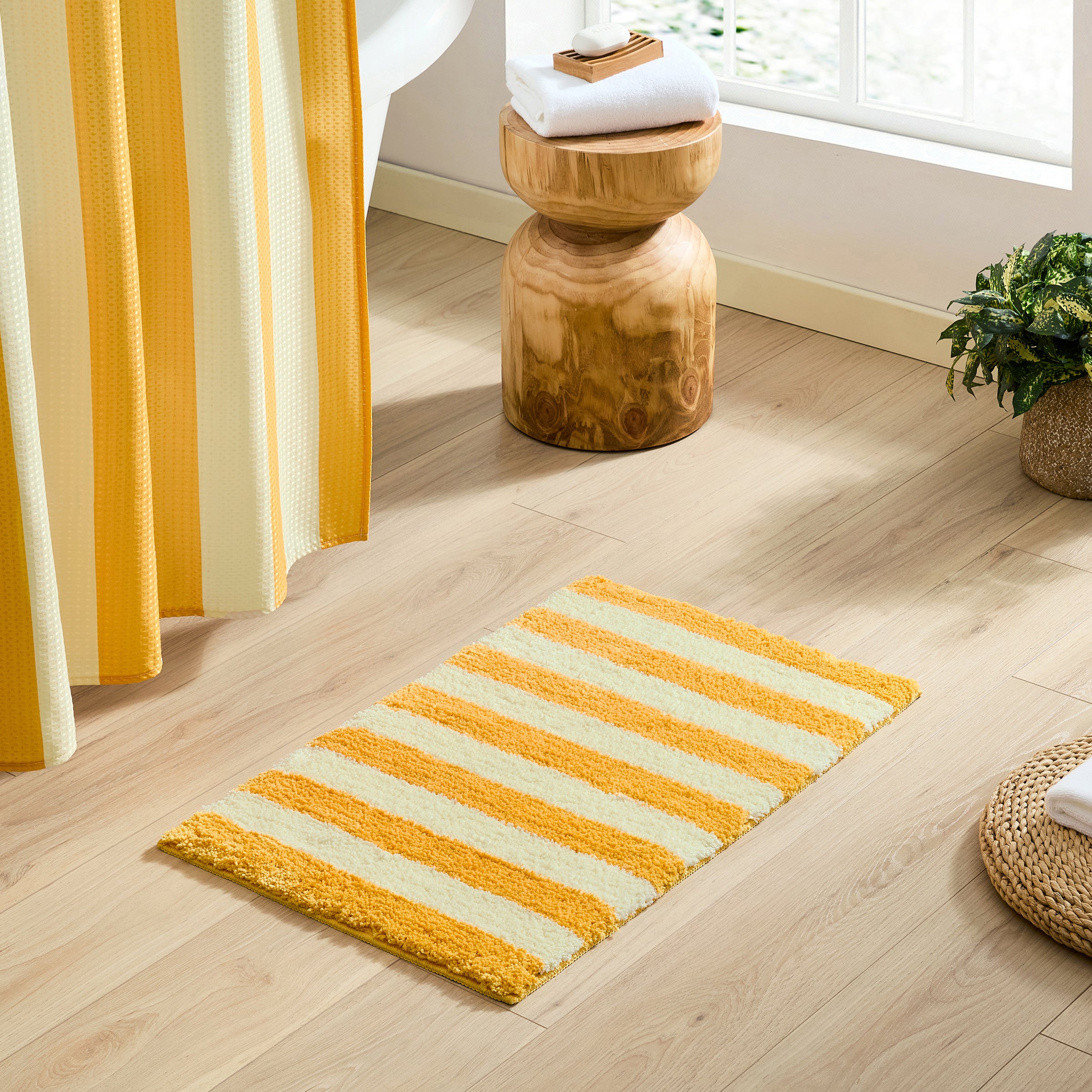 Yellow and white striped rug on a wooden floor with a wooden stool and plant in the background.
