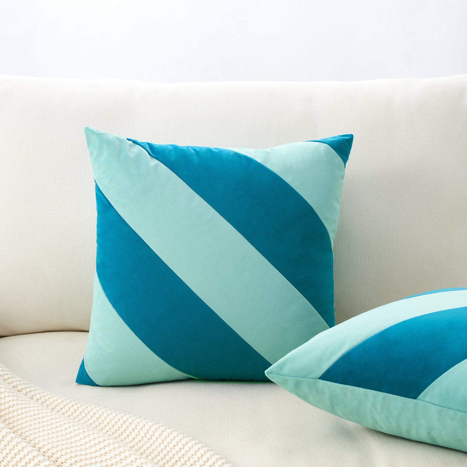 Two blue and green striped pillows on a beige couch.