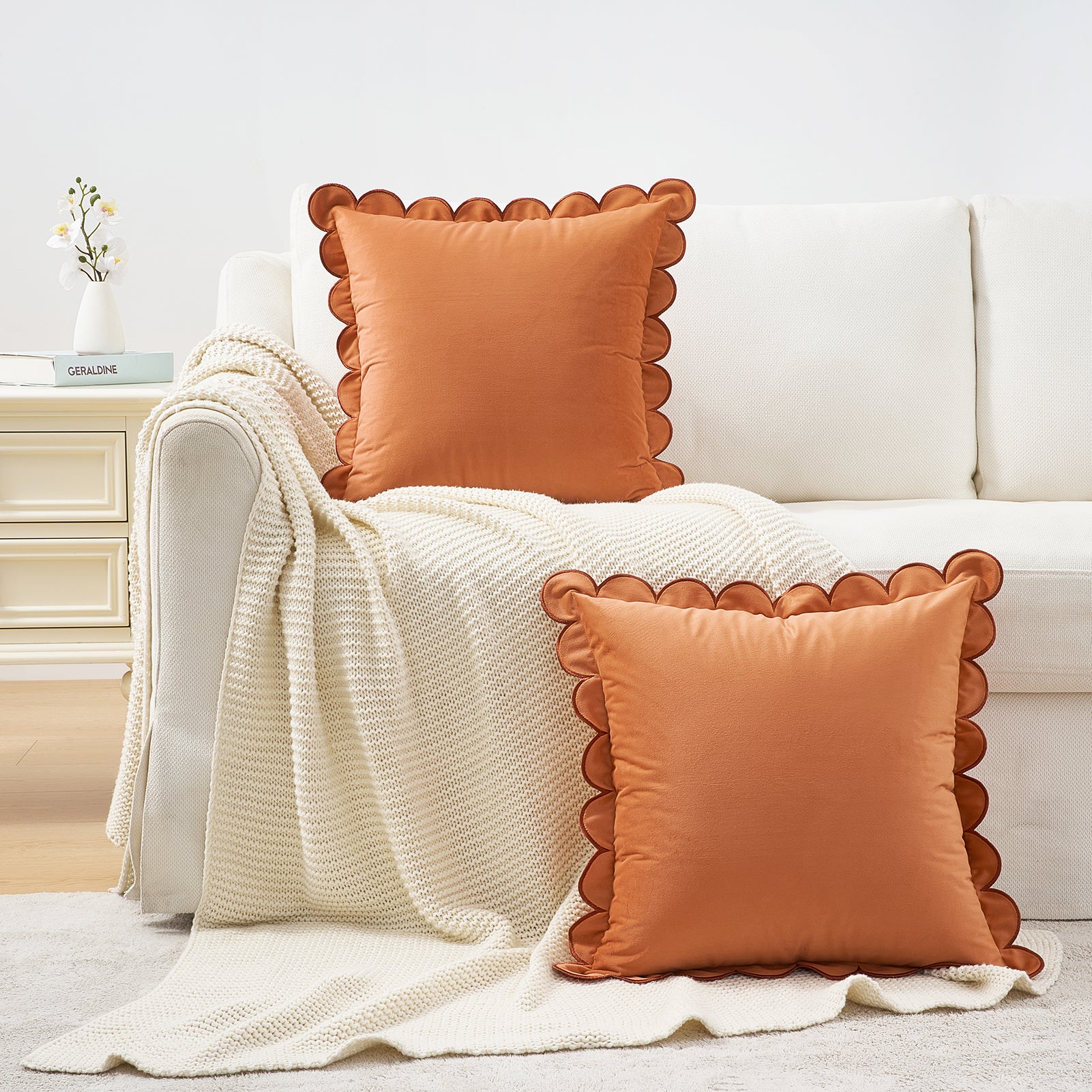 Orange pillows with scalloped edges on a white sofa with a beige blanket.