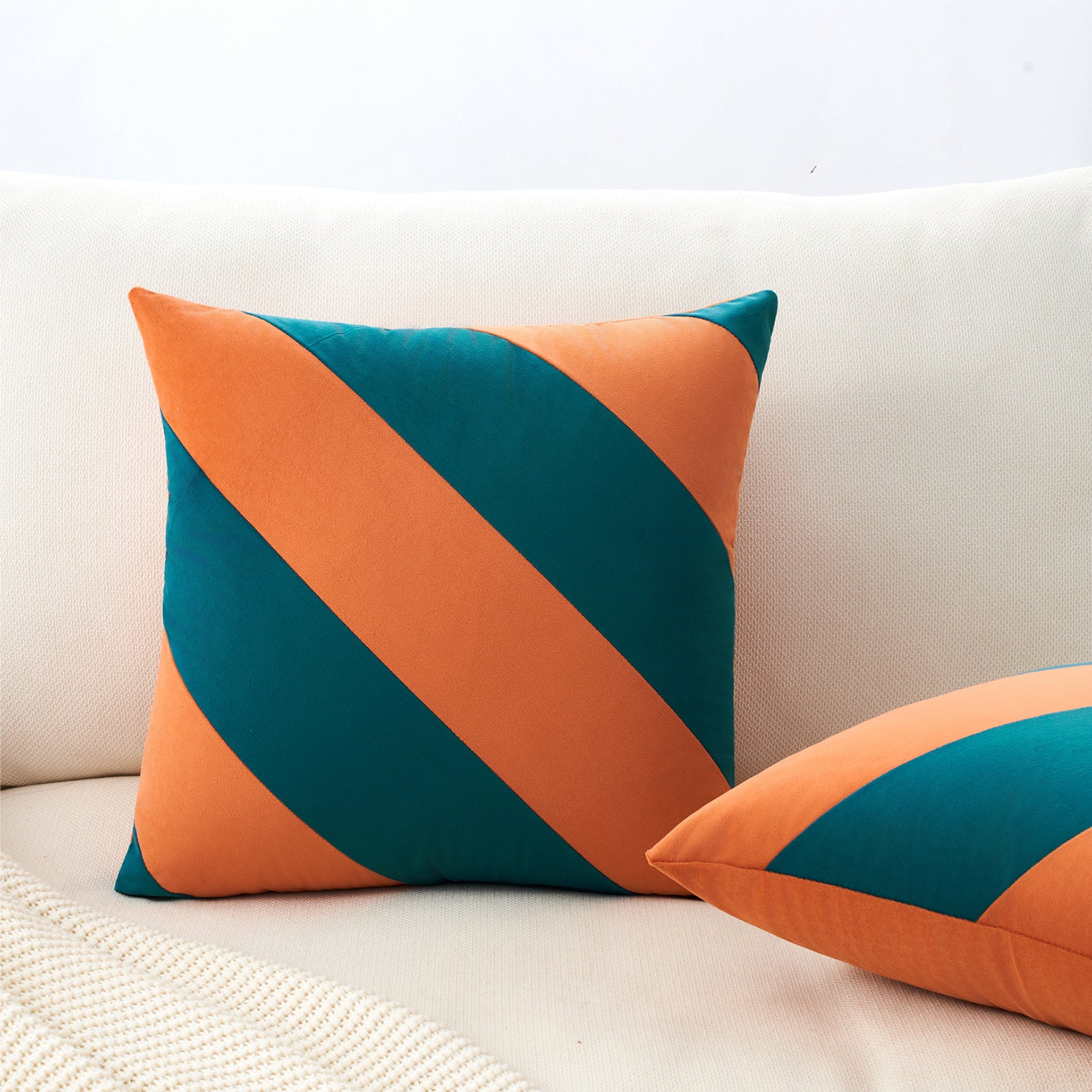 Two decorative pillows with orange and teal stripes on a white couch.