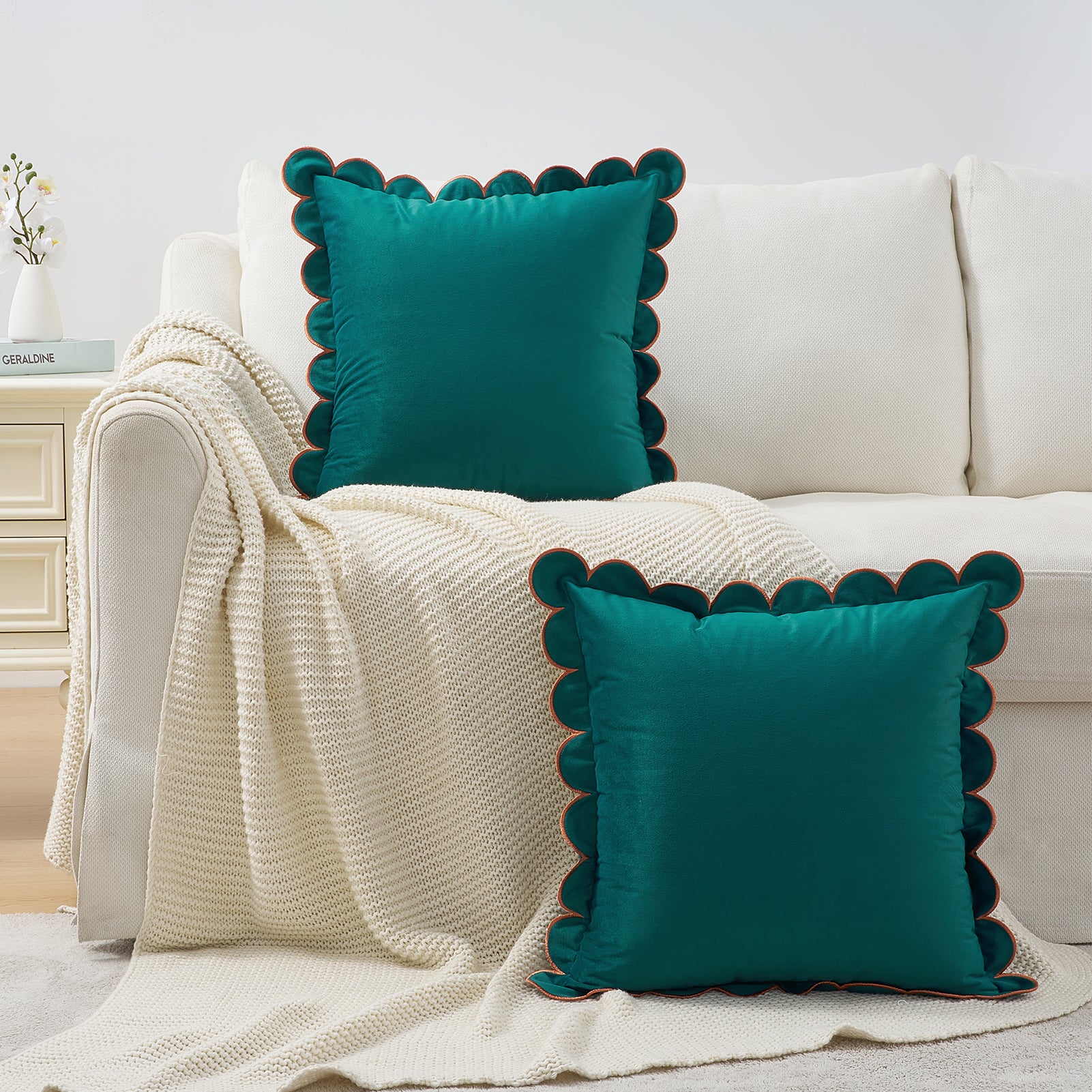 Teal pillows with scalloped edges on a white sofa with a beige blanket.